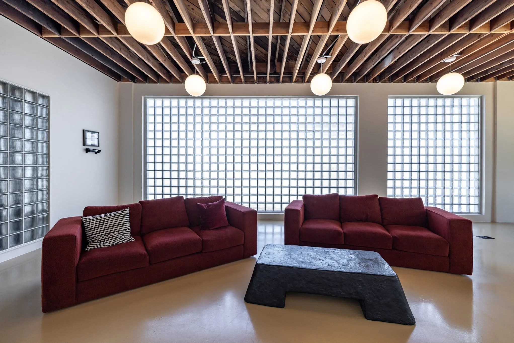 Modern living room with two red sofas, a black stone coffee table, large glass block windows, and a wooden ceiling with spherical ceiling lights.