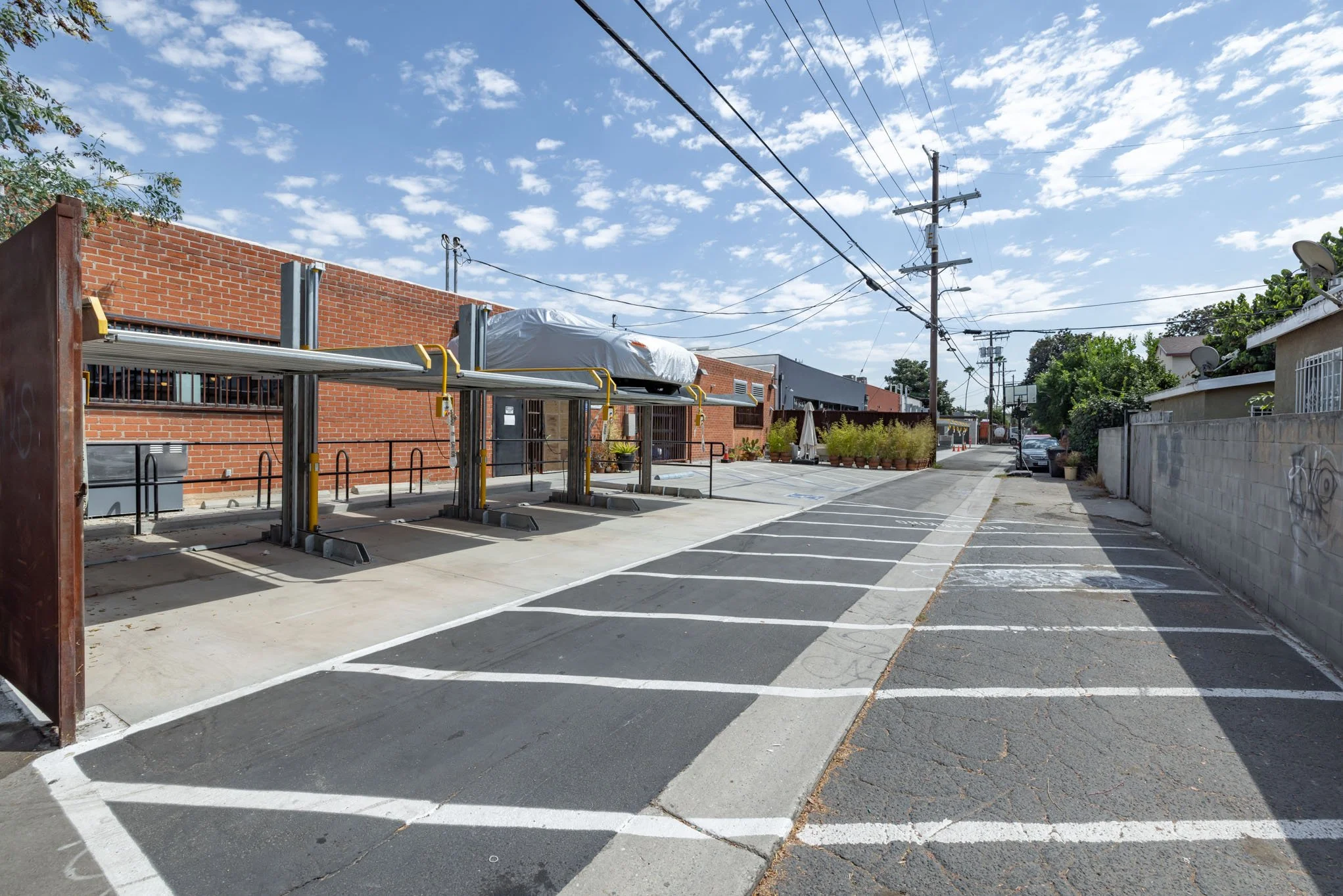 Empty parking lot with designated parking spaces, brick building, utility poles with power lines, and a clear sky with scattered clouds.