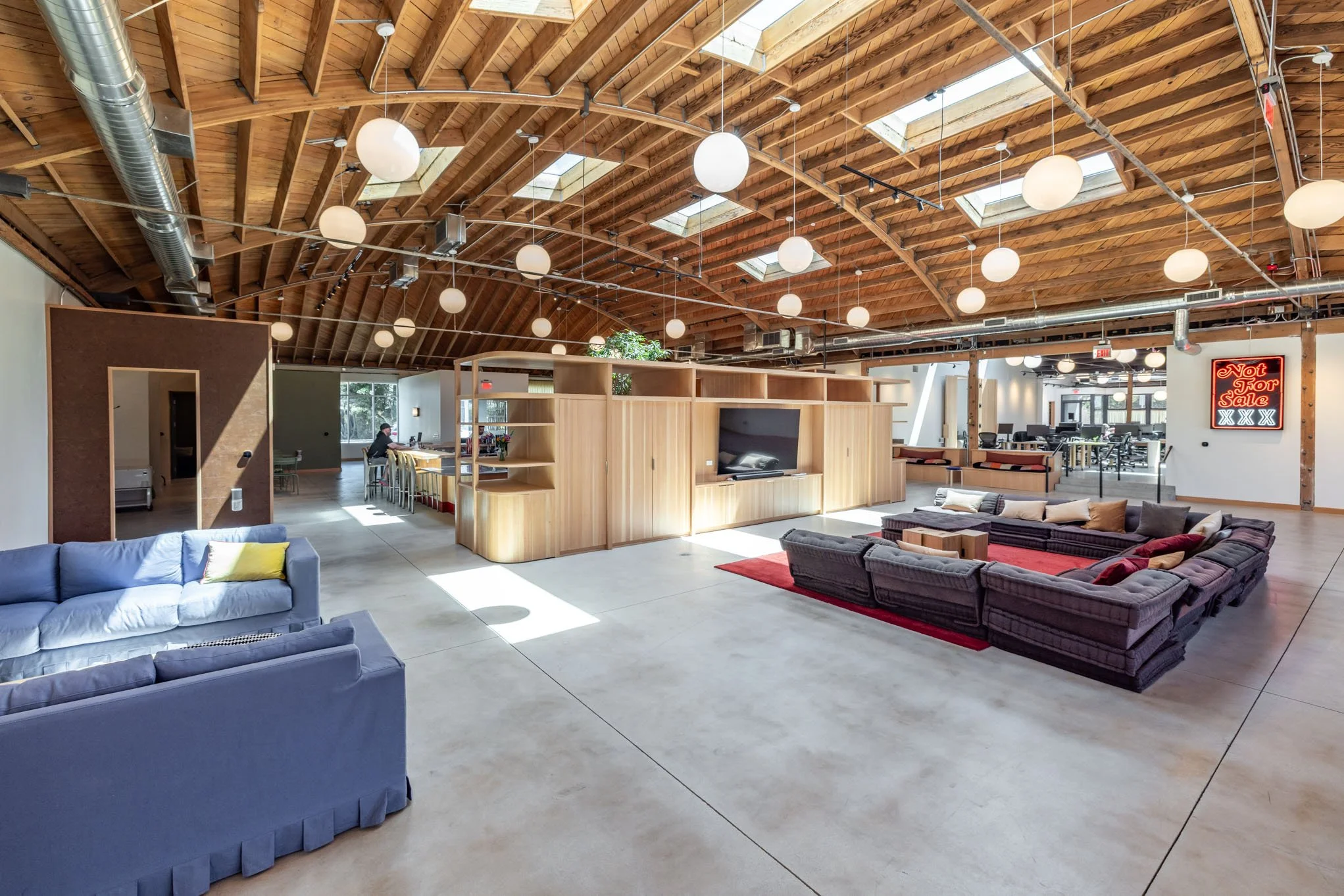Spacious modern open-plan office lounge area with couches, a TV, wooden partition, and a sign that reads "Not for Sale".