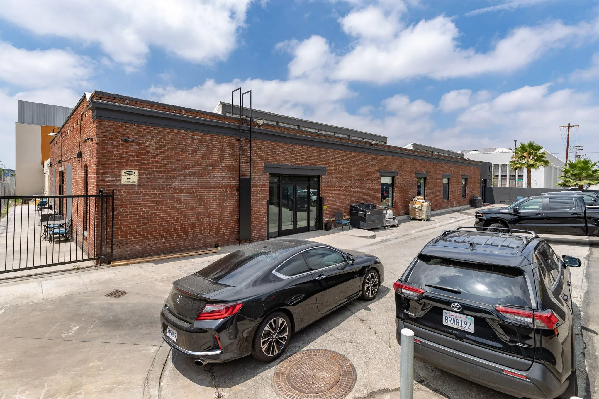 Parking lot with three cars parked in front of a red brick building under a partly cloudy sky.
