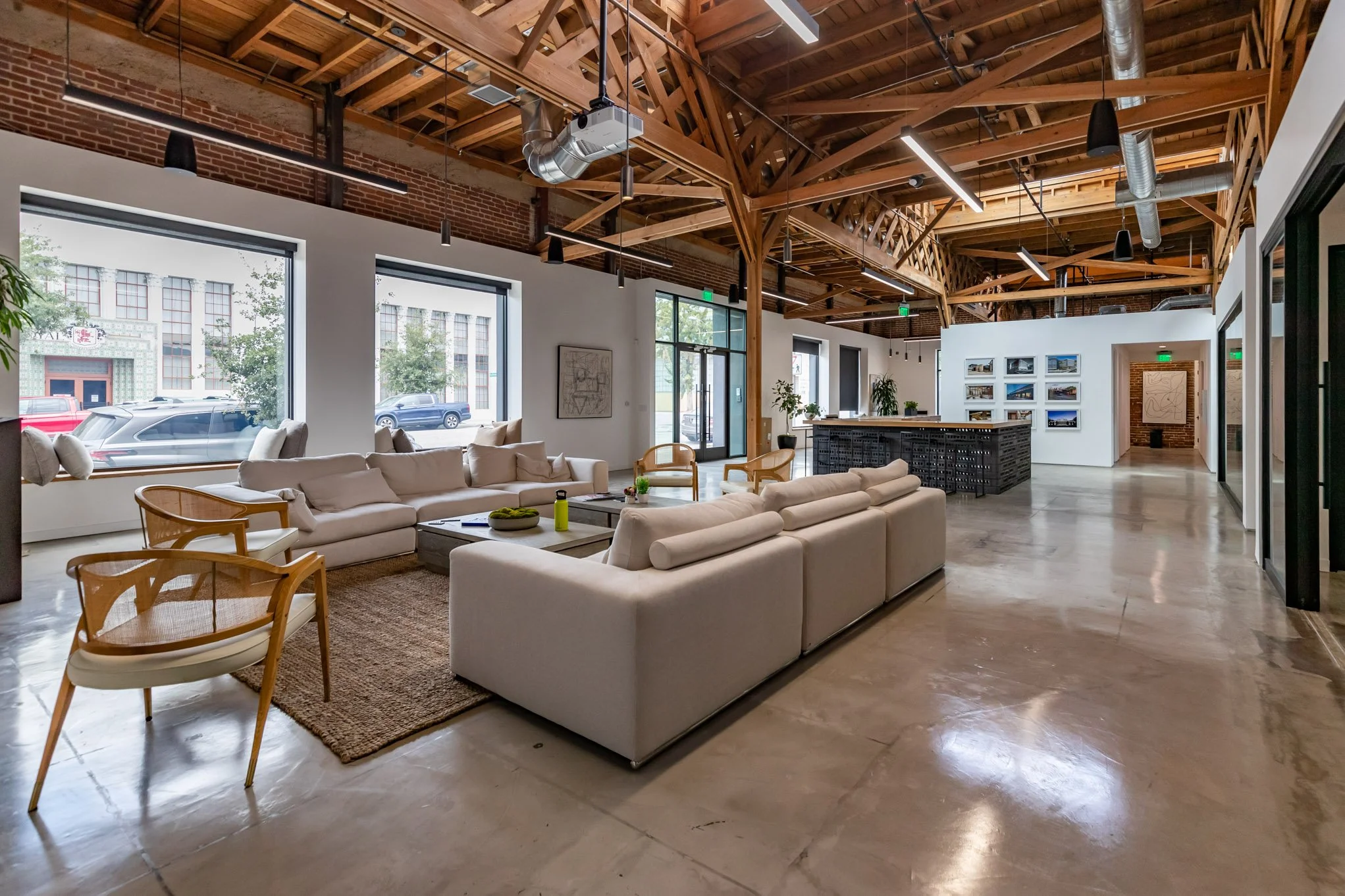 Spacious modern loft with white sofas, wooden chairs, large windows, and exposed wooden beams in the ceiling.