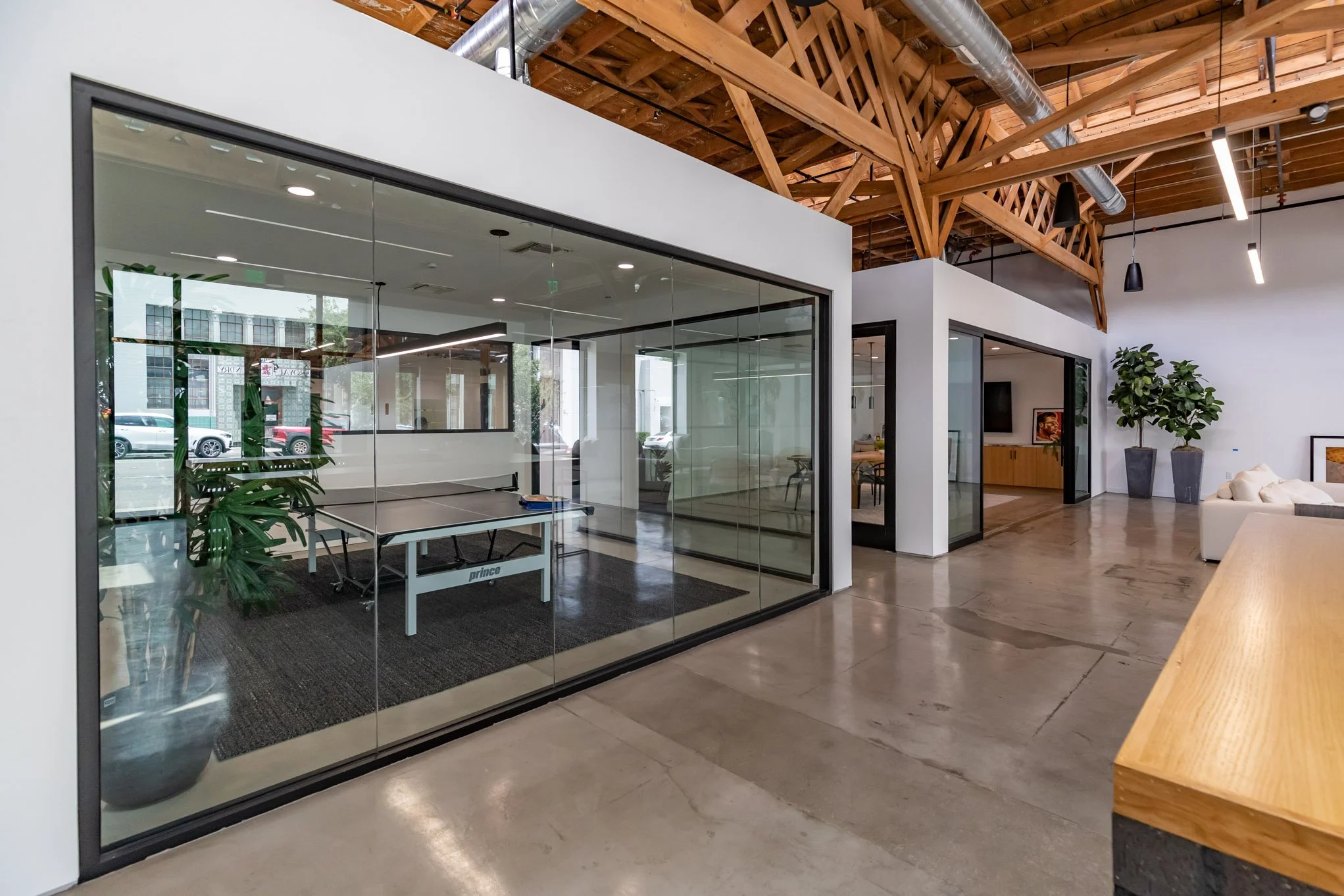Modern office interior with glass walls, ping pong table, potted plants, and seating area.