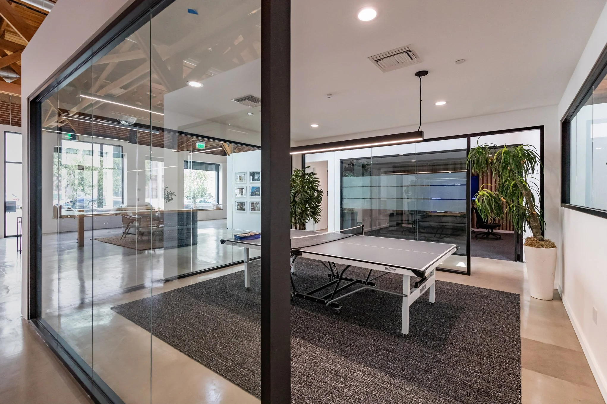 Modern office space with a ping pong table, glass walls, and indoor plants.