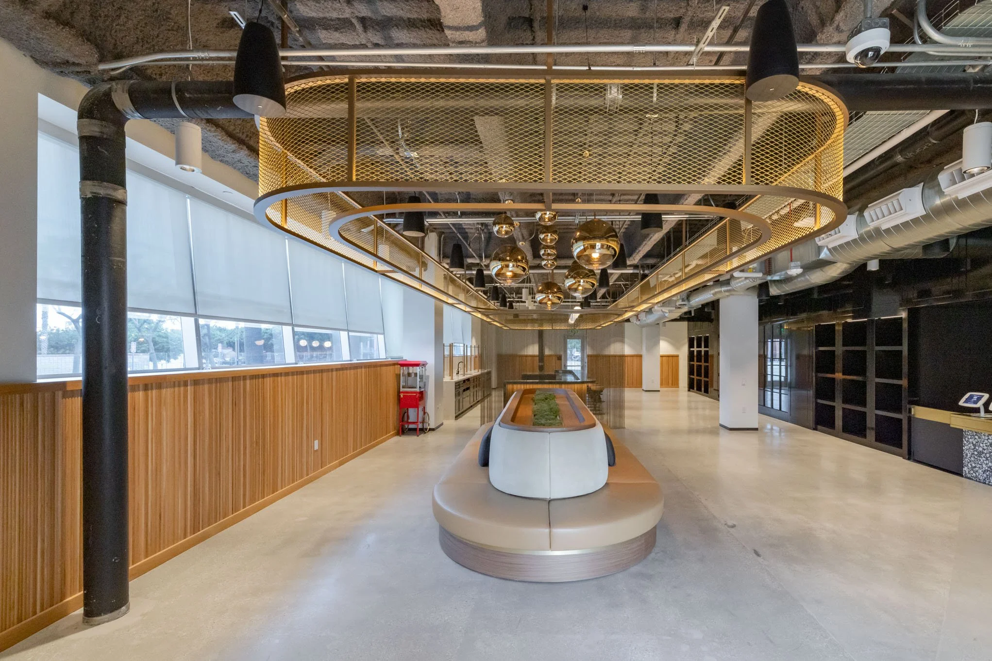 Empty modern lobby area with large windows, wooden wall paneling, a bench in the center, and black and gold decorative ceiling fixtures.