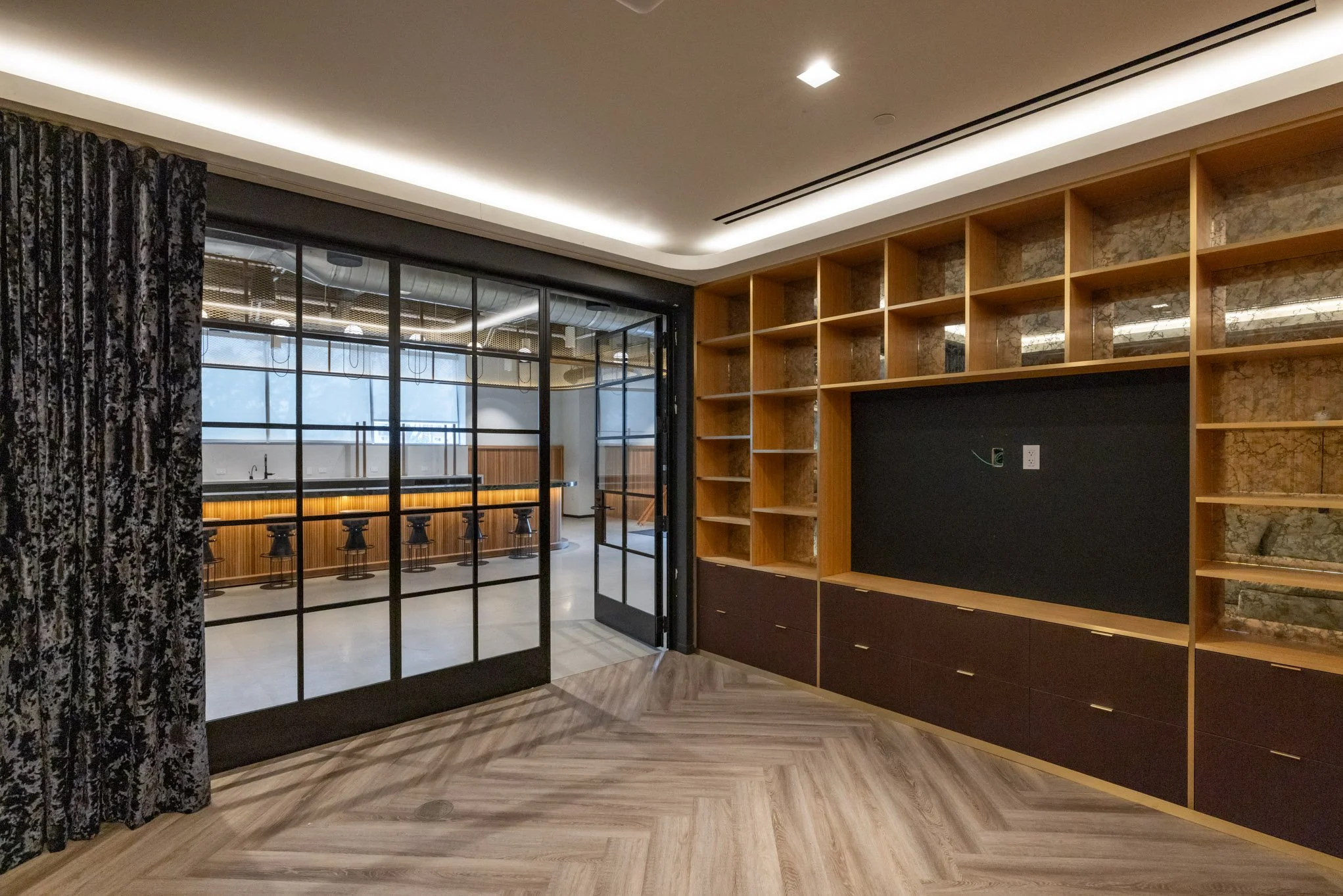 Modern home interior with built-in wooden shelves, black wall panel, glass sliding door, and view into kitchen with bar seating.