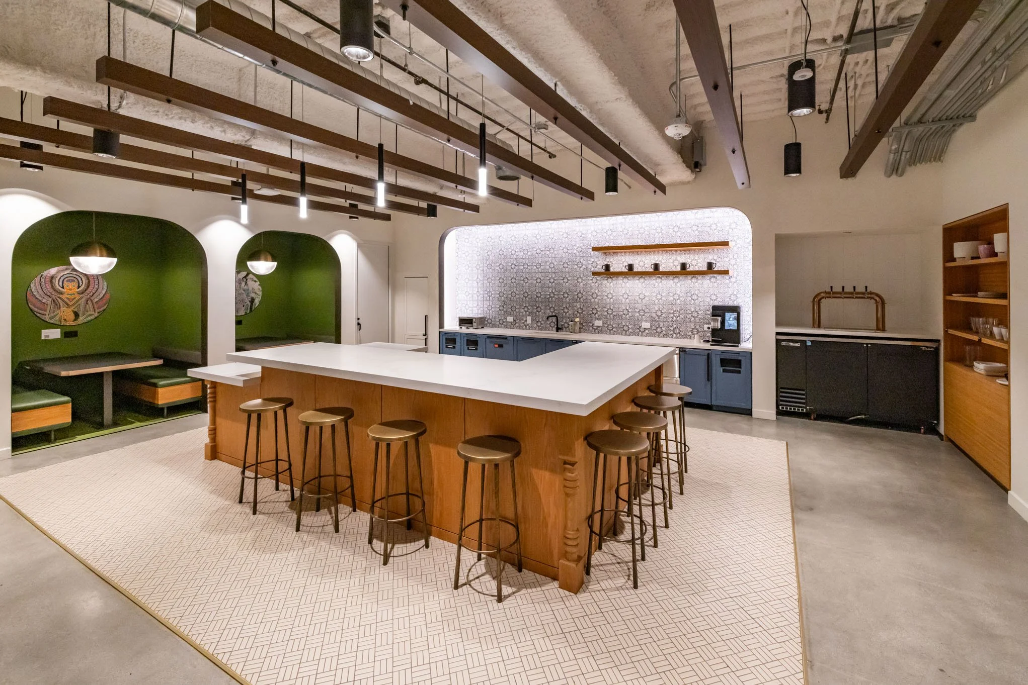 Modern kitchen with a central white island, brown stools, blue cabinetry, patterned backsplash, green nook seating areas, and wooden shelving.