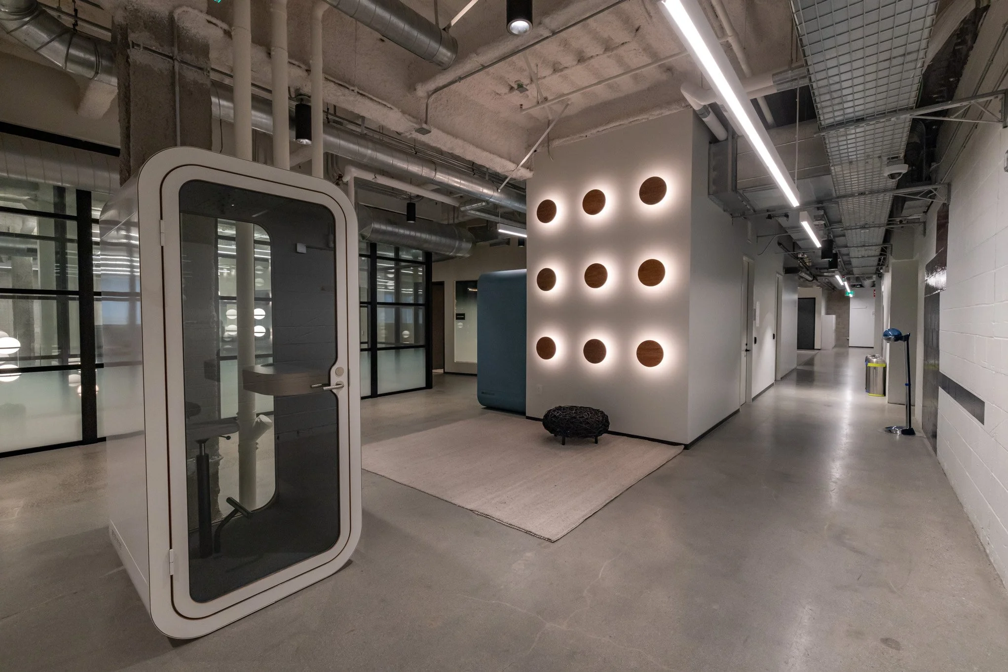 Modern office hallway with a telephone booth, a geometric wall with circular cutouts, and sleek lighting.