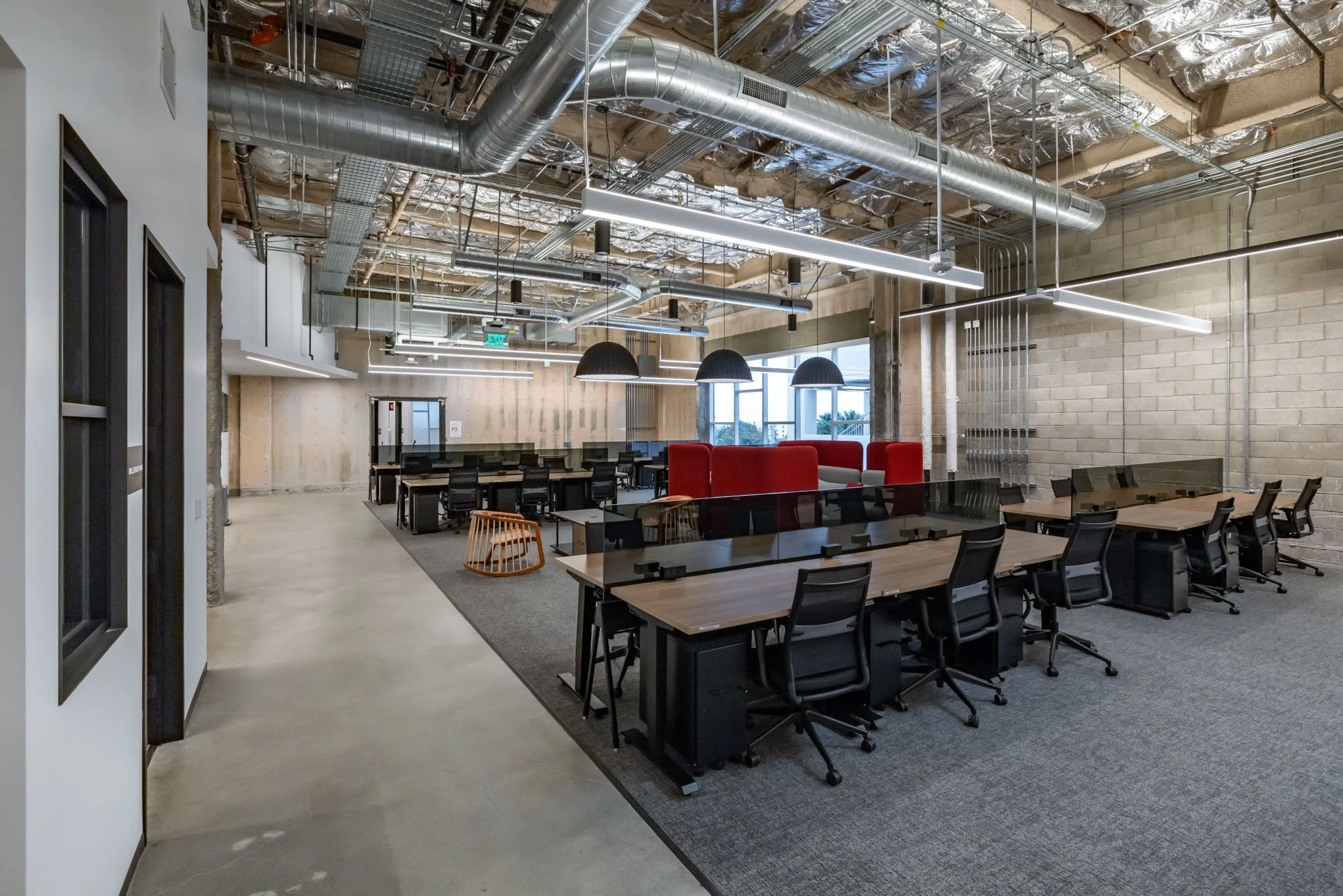 Open office space with modern design, exposed ceiling with ductwork and piping, multiple workstations, and large windows