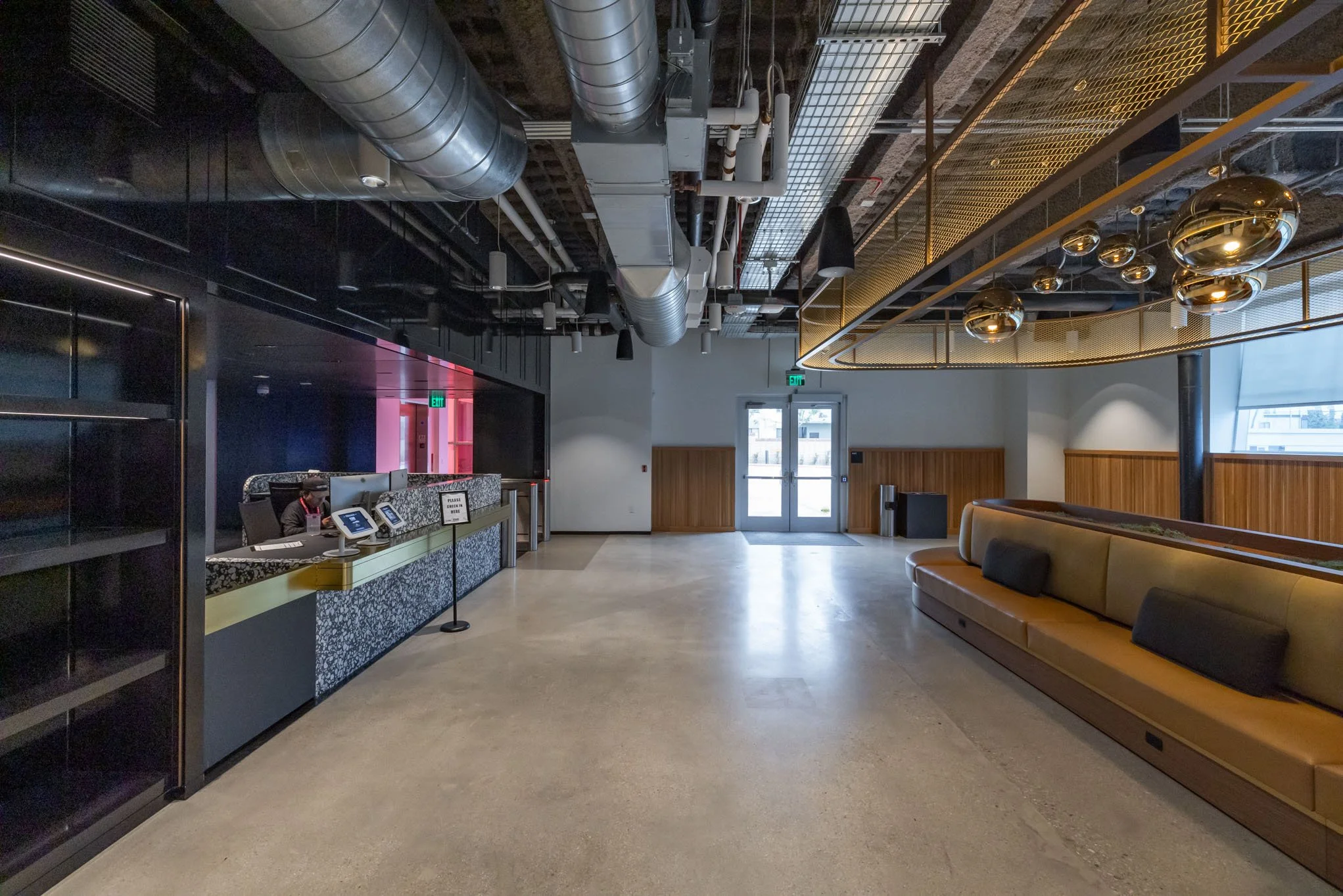Empty lobby or reception area with modern seating, industrial ceiling, and a front desk with a person working.