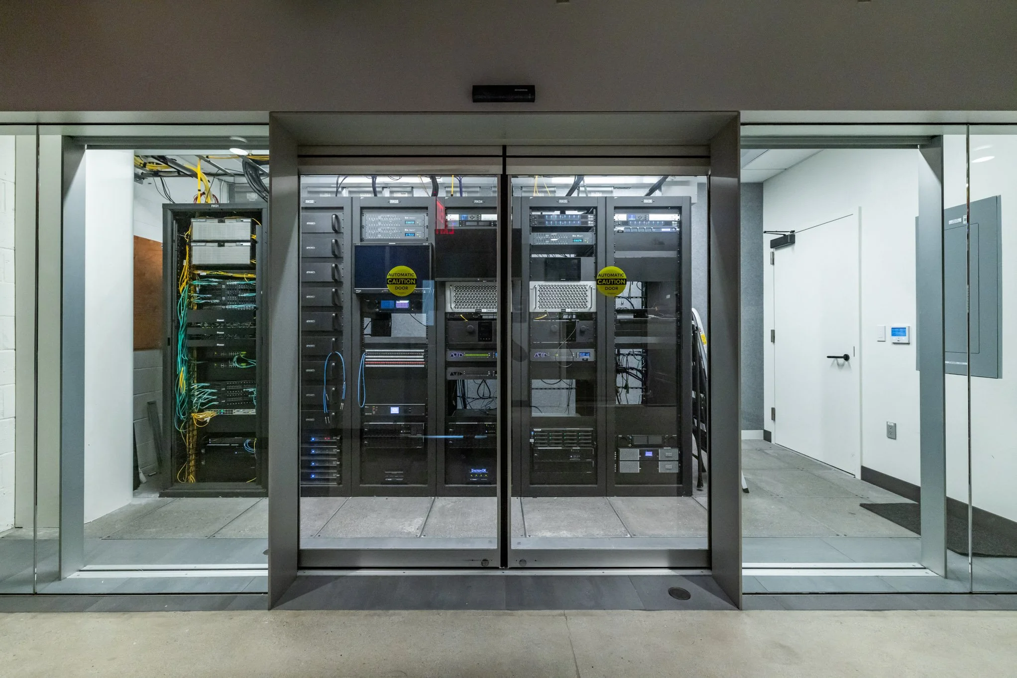 Server racks with computer equipment inside a data center, viewed through glass doors.