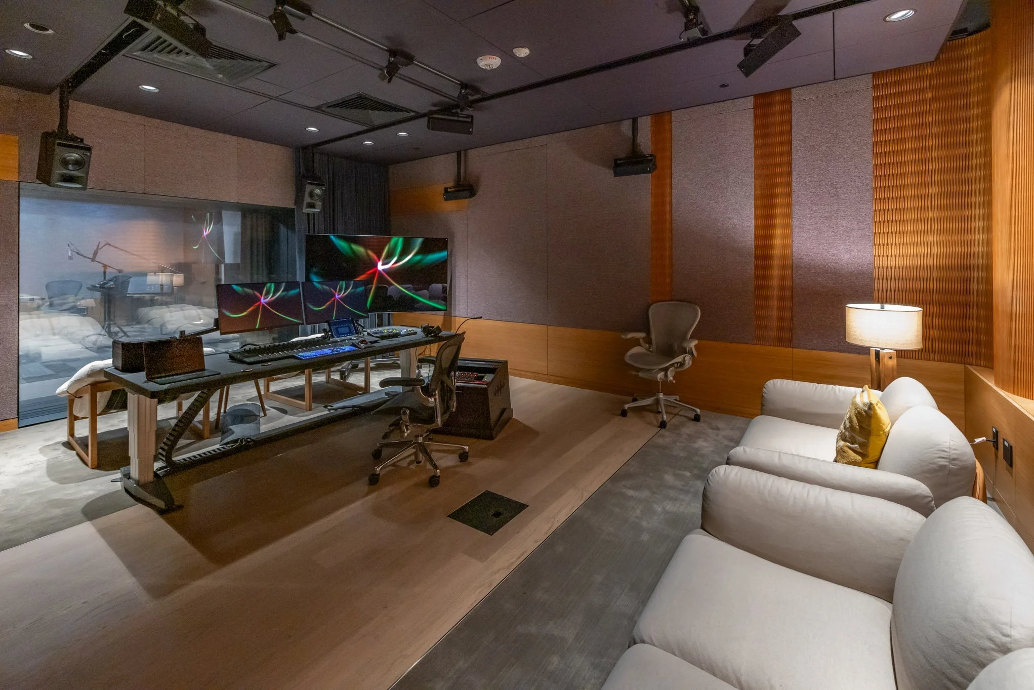 Interior of a professional music or recording studio with multiple monitors, a control desk, chairs, a sofa, and soundproof walls.