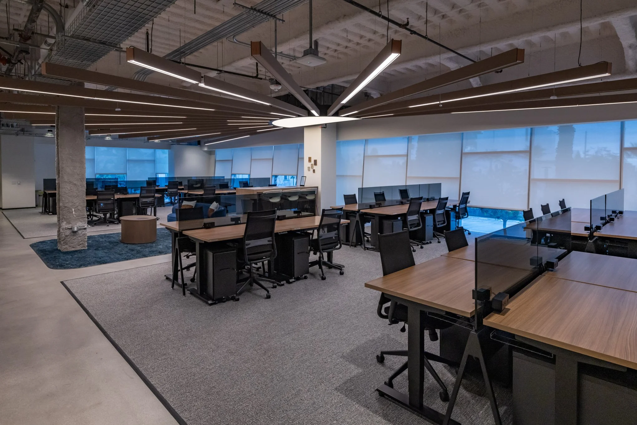 Modern shared office space with multiple workstations, office chairs, and large windows with blinds.