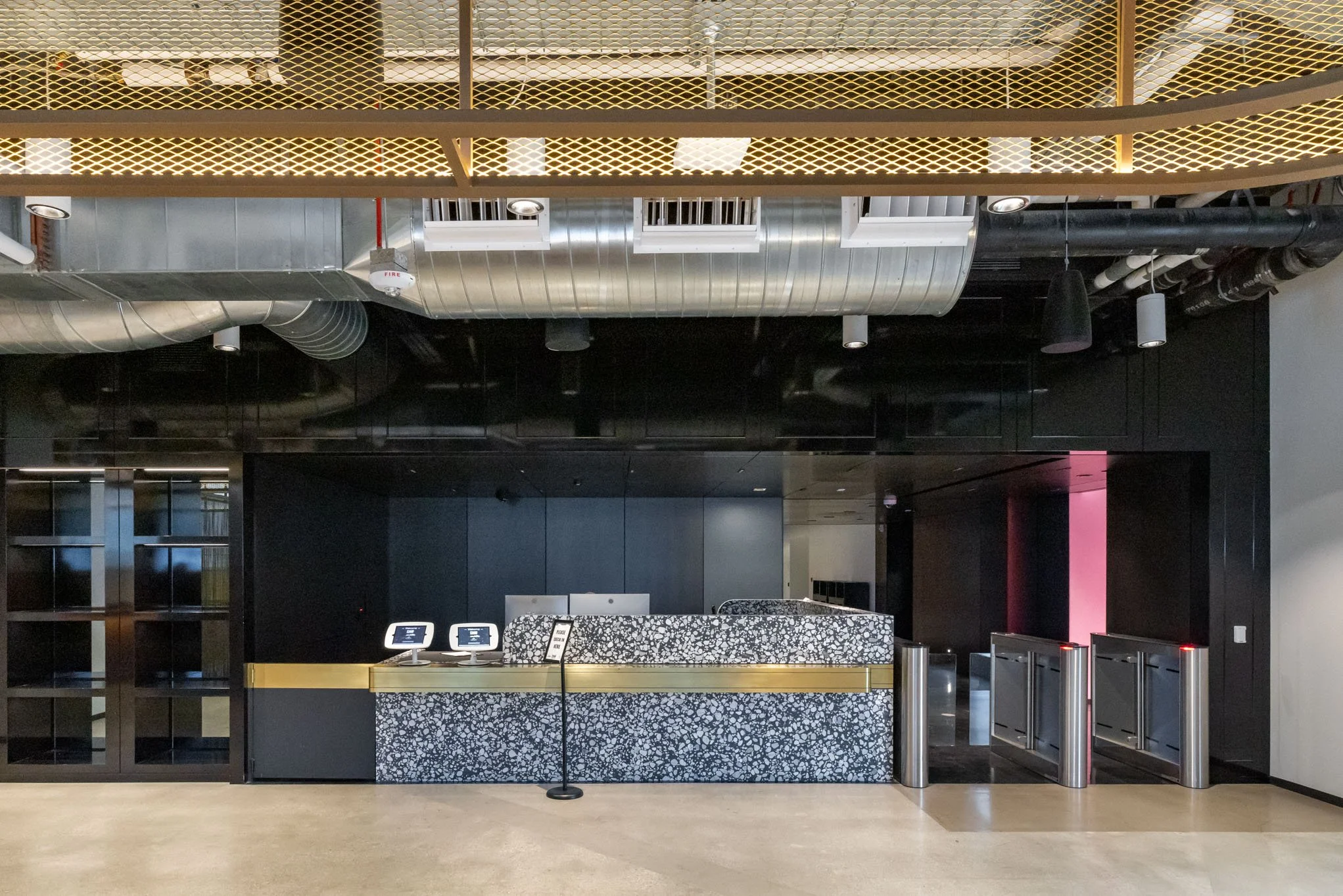 Modern building interior with reception desk, black walls, exposed ductwork, and turnstiles.