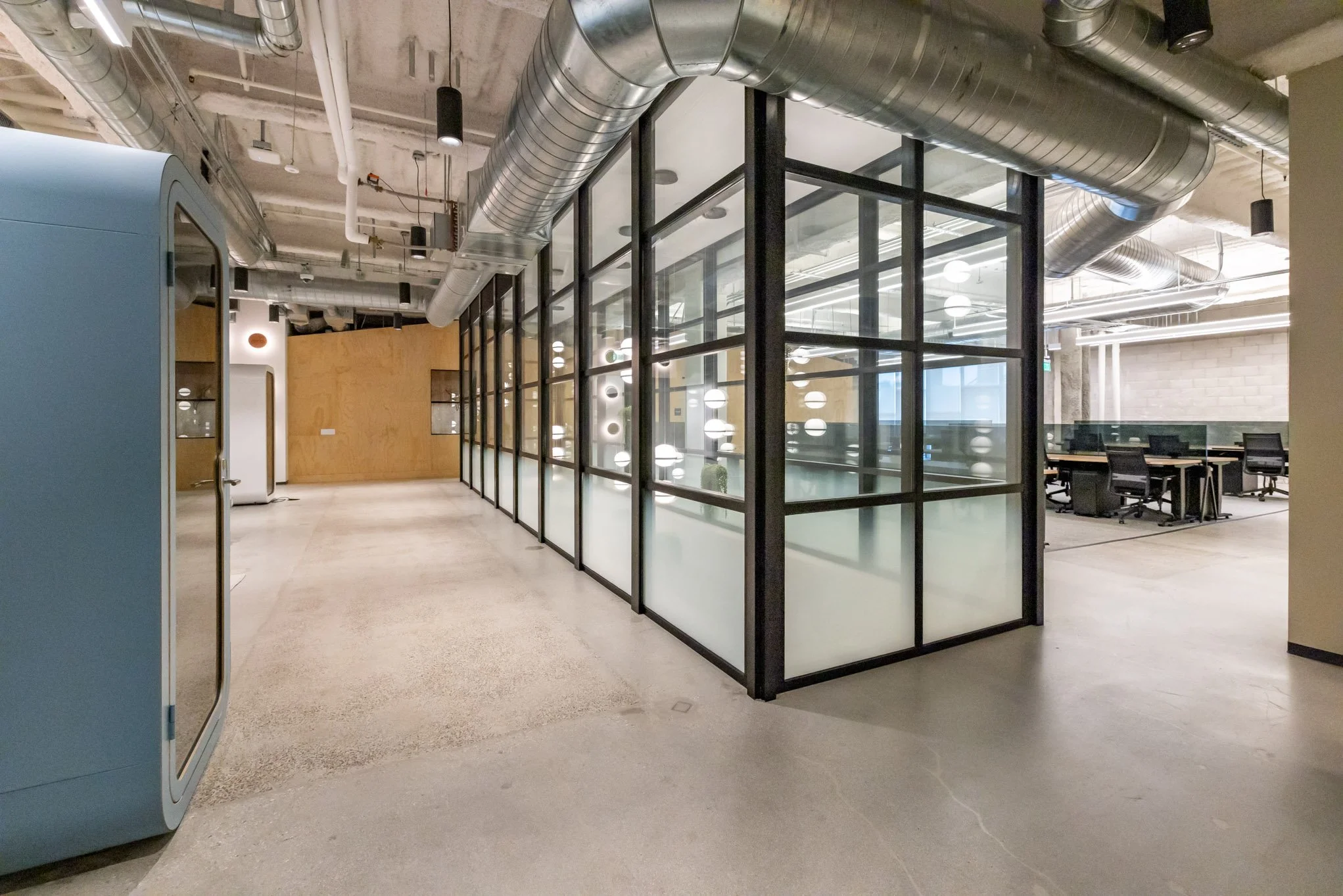 Modern office space with glass-walled conference rooms, exposed ductwork, and workstation area with chairs and desks.