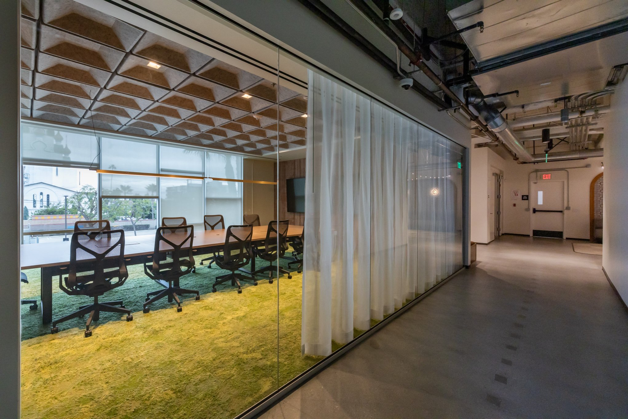 Empty conference room with a long table and ergonomic chairs, viewed through glass walls with curtains in a modern office building.