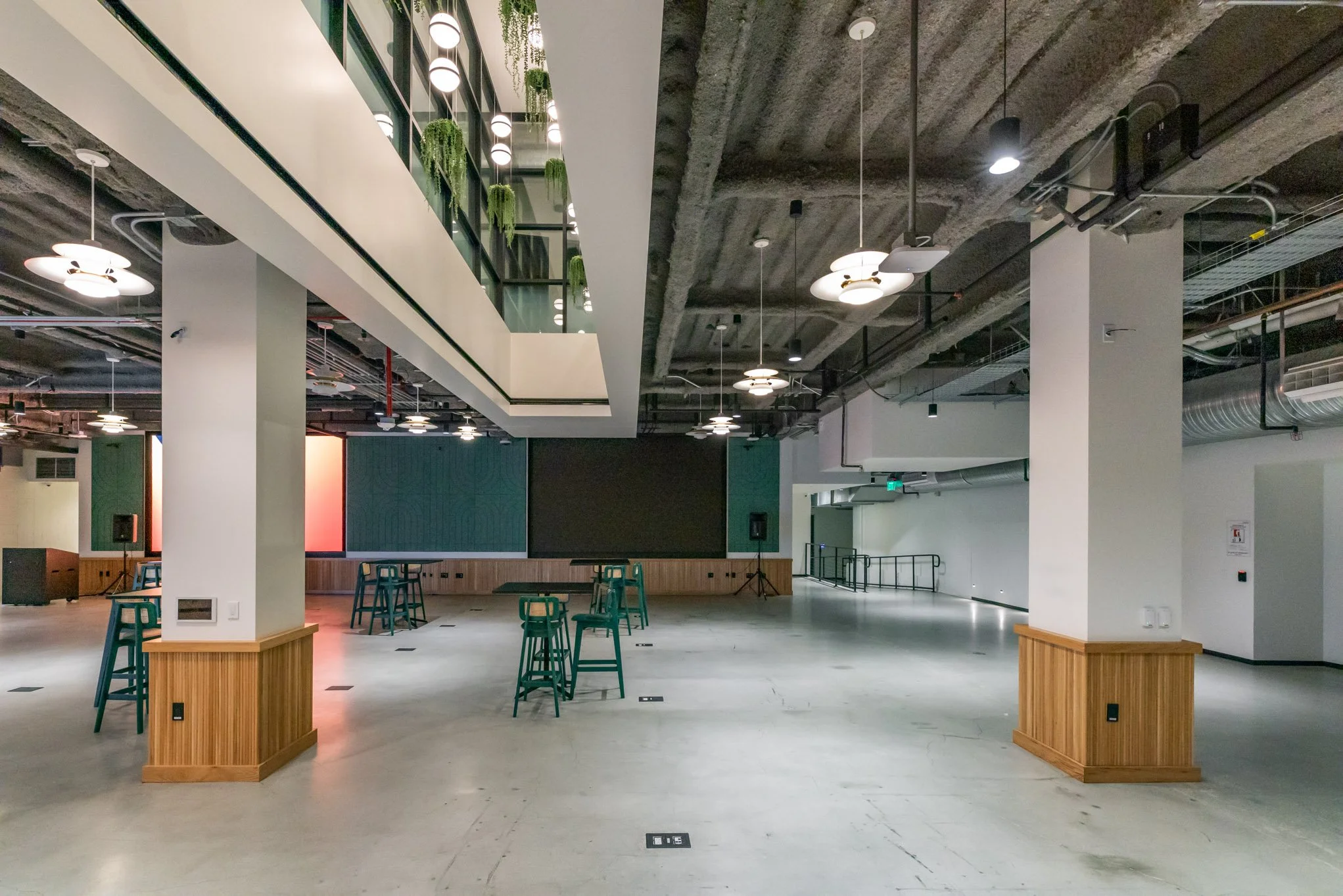 Empty indoor space with high ceilings, hanging light fixtures, and scattered tall chairs, featuring modern decor and a mix of modern and industrial design elements.