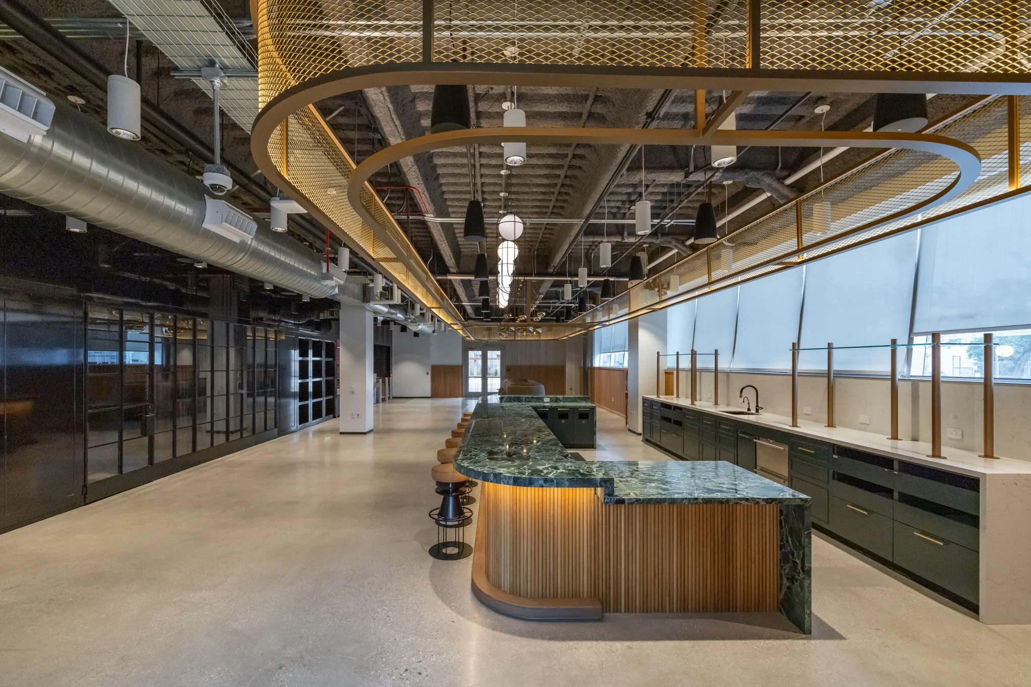 Interior of a modern, open-concept space with a curved green marble countertop, bar stools, large windows, and industrial ceiling design.