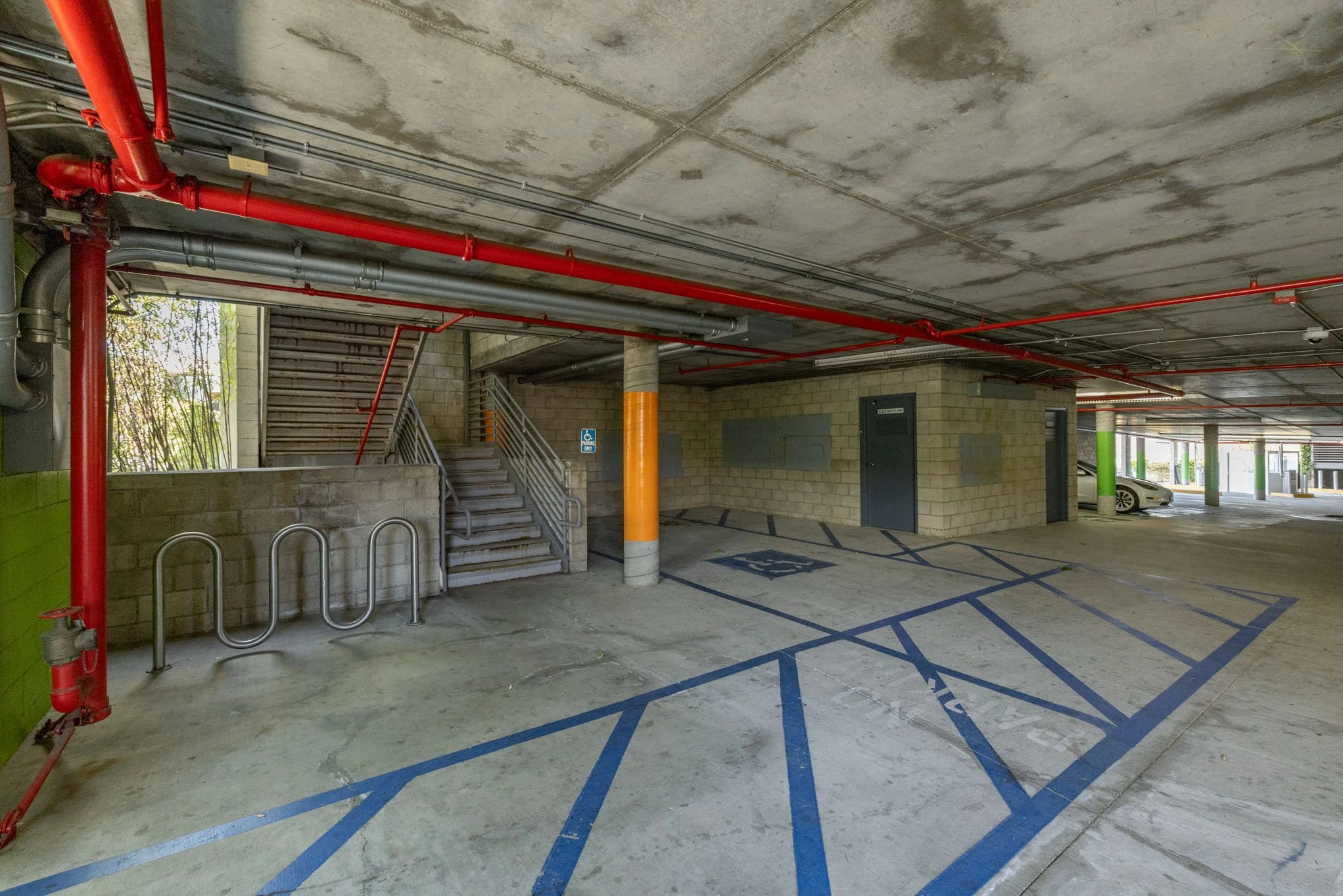 Underground parking garage with parking spots, including disabled parking, pipes and stairs leading upward.