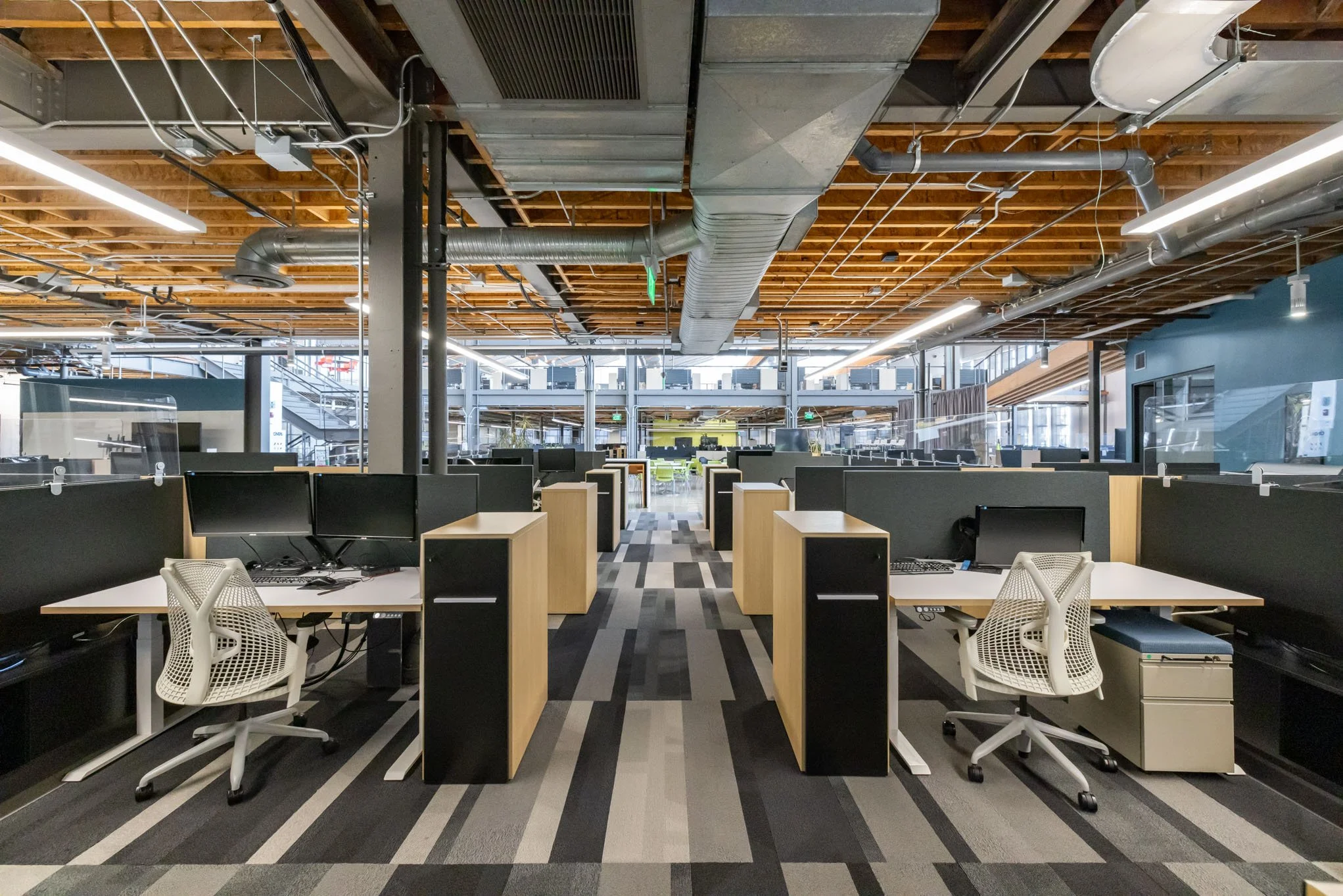 Empty open-plan office with rows of desks, computer monitors, and ergonomic chairs.