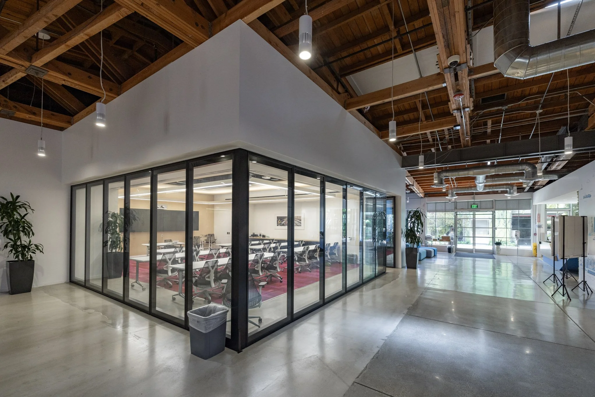 Modern office space with a glass-walled conference room, open seating area, and natural light from large front windows.