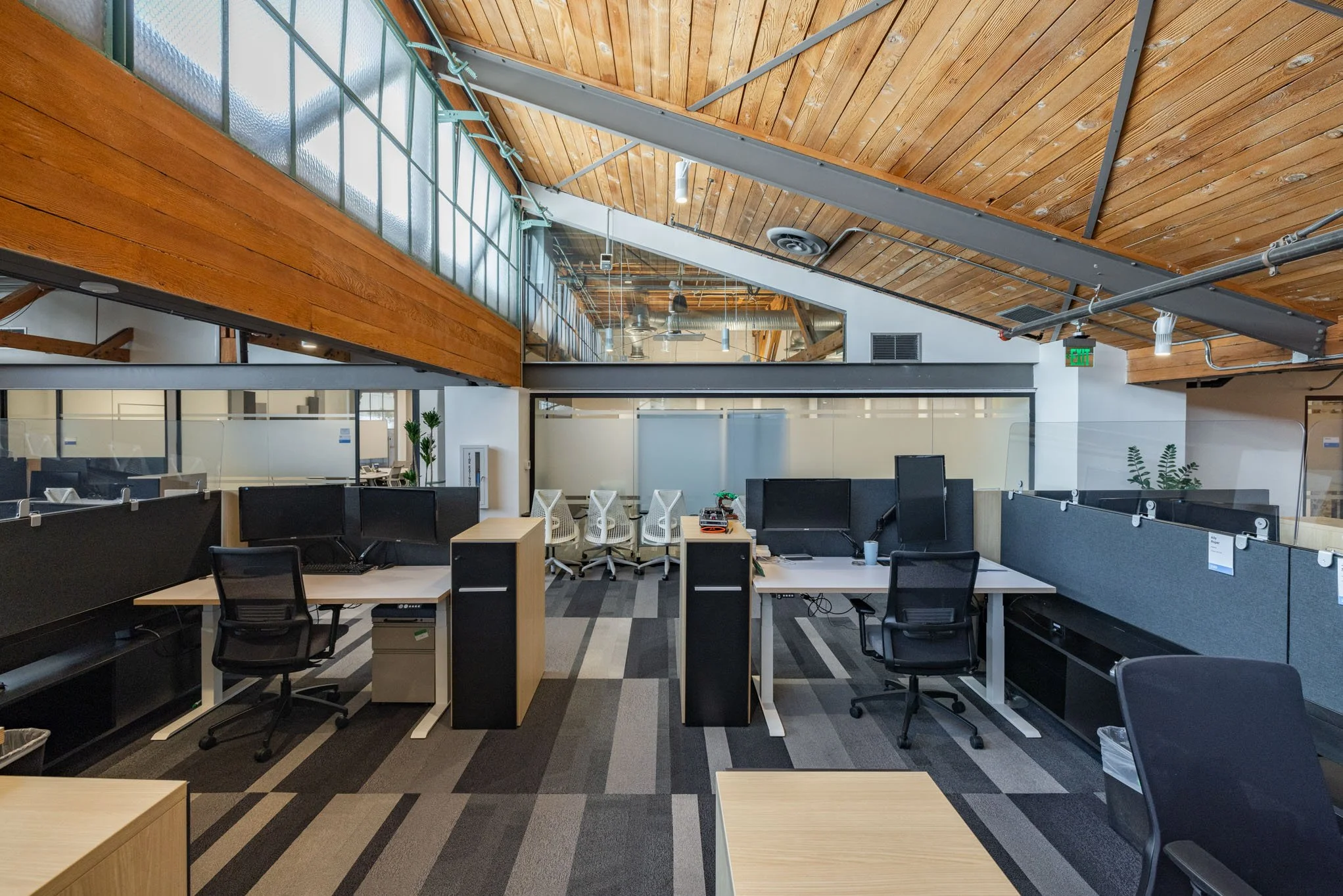 Office space with workstations, cubicles, glass partitions, and a wooden ceiling with exposed beams.