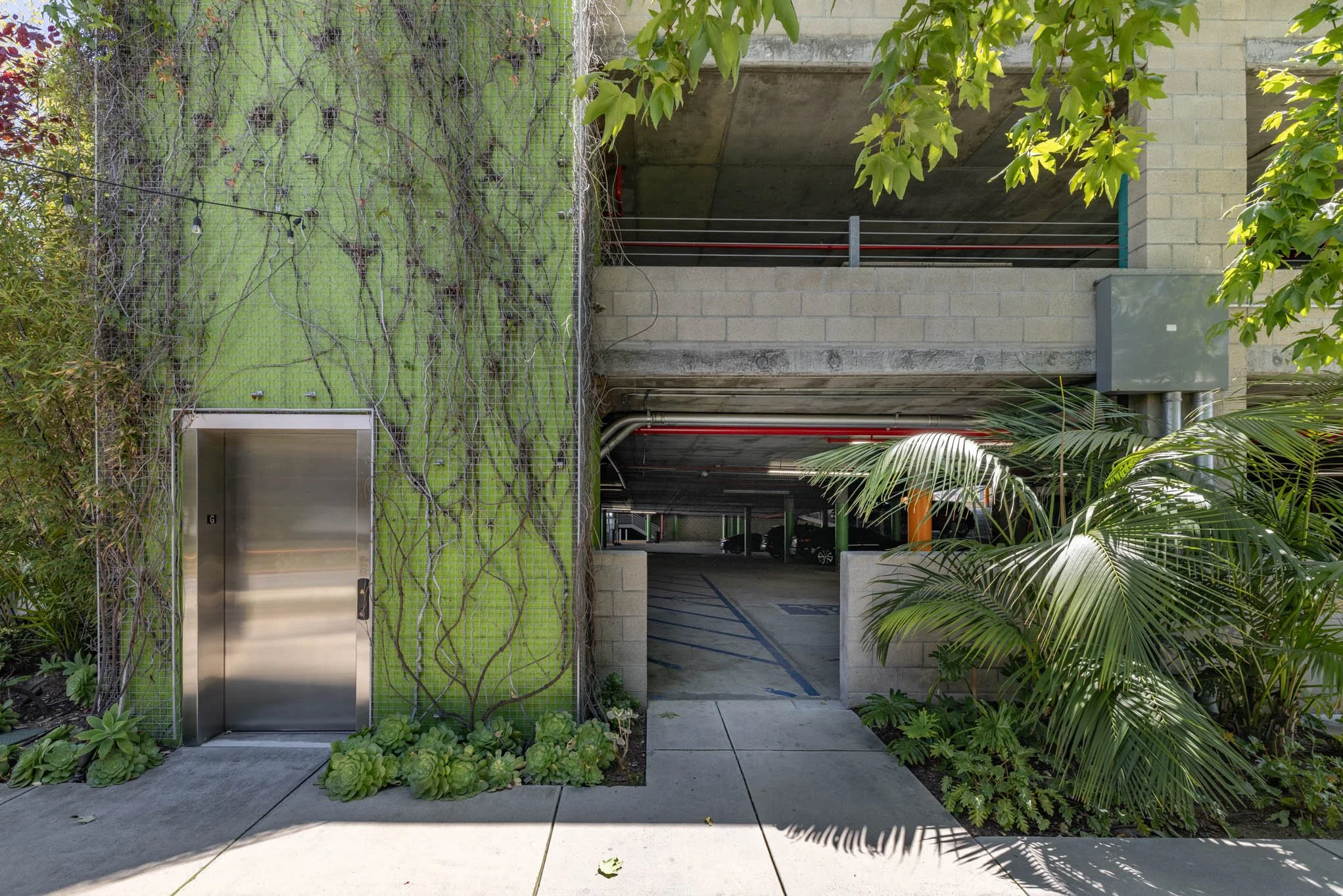 Entrance to underground parking garage with green vertical garden and plants on either side, concrete and brick structure, and a small alley leading into the garage.