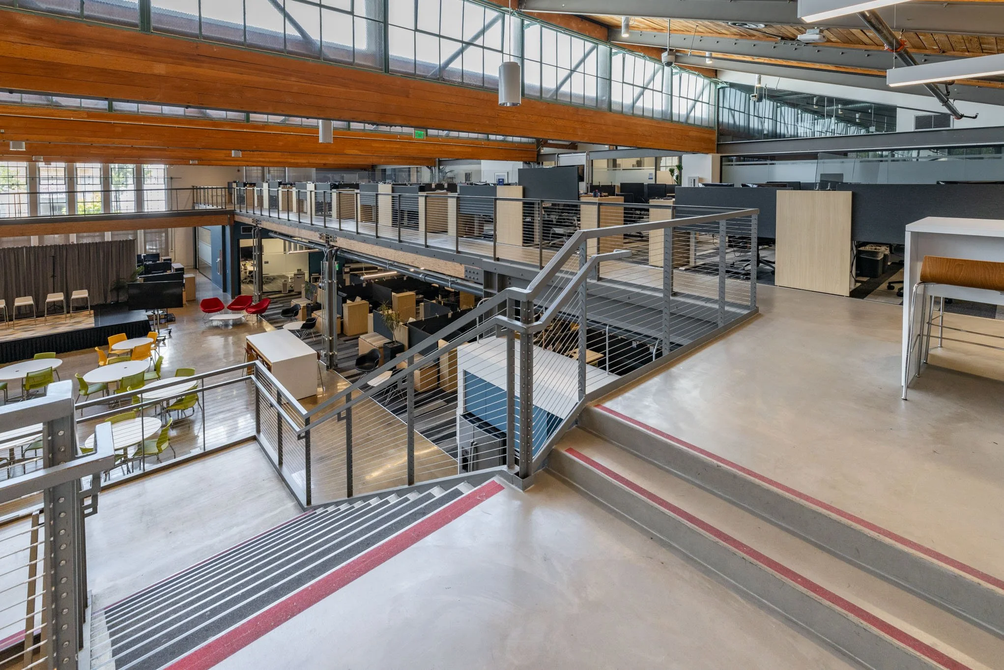 Interior of a modern multi-level office space with stairs, open workspaces, curtains, and colorful chairs.