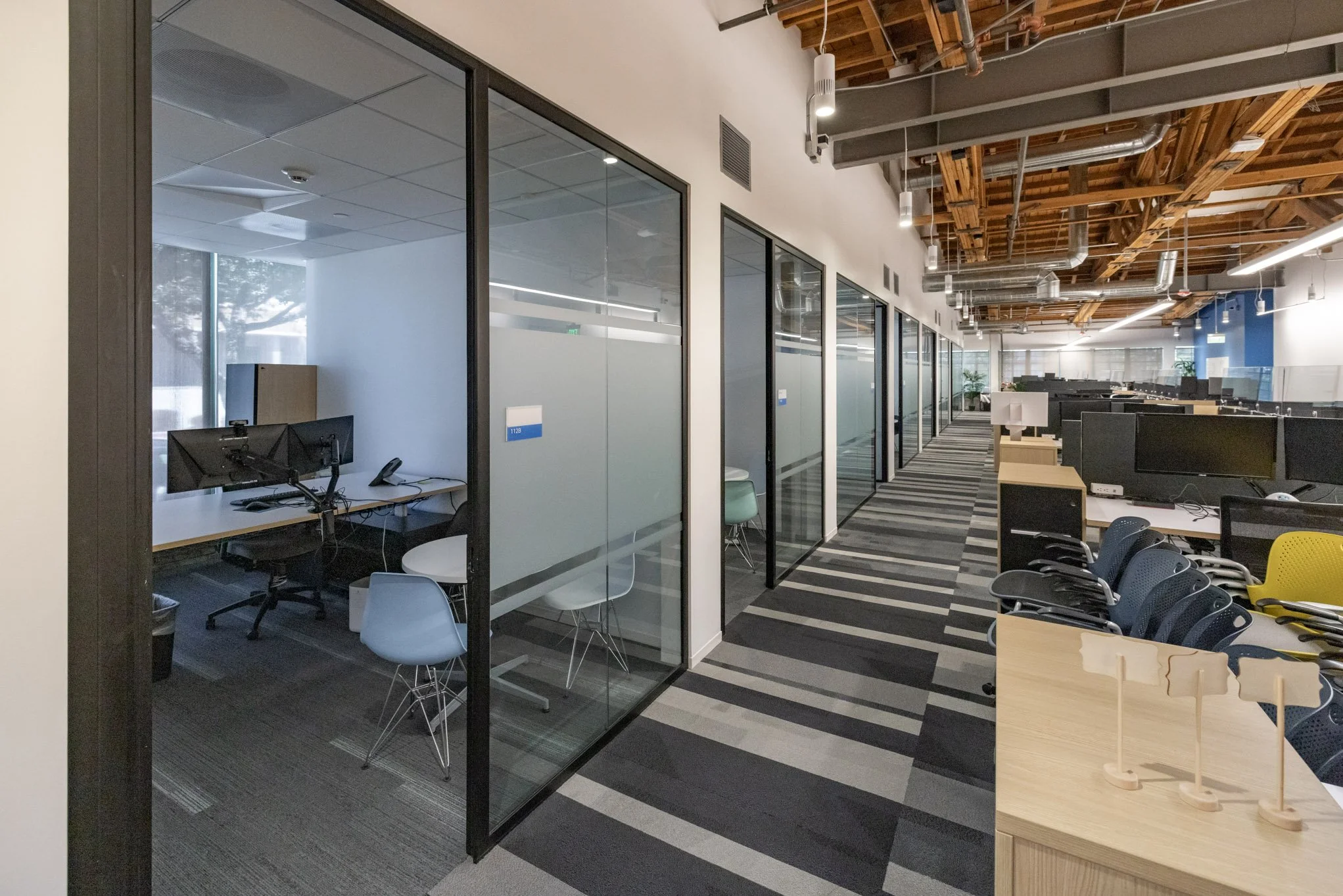 Modern office with glass-walled conference rooms, open workstations, and a patterned carpet in shades of gray and beige.