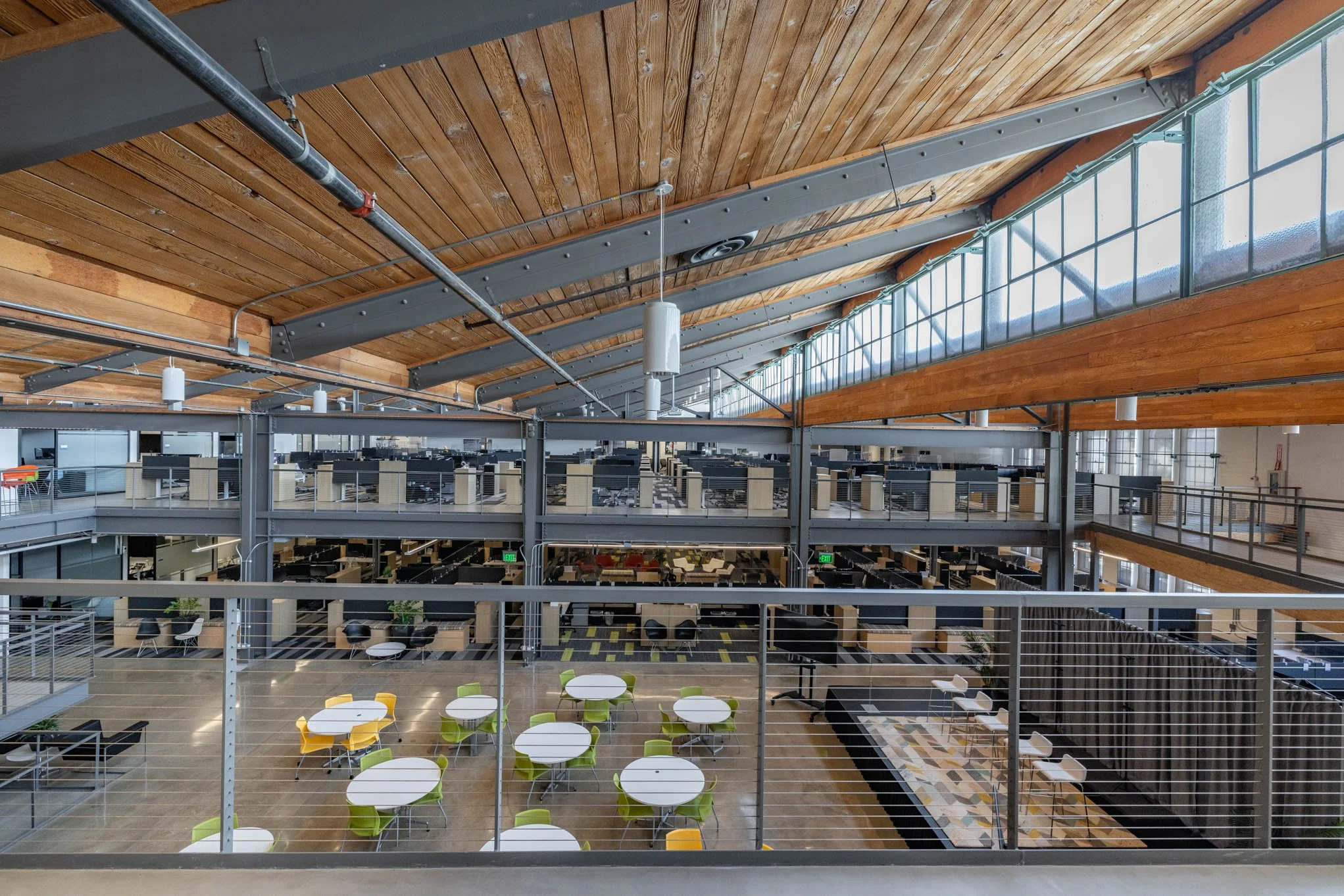 Interior of a modern office with an open layout, multiple workstations on multiple floors, and a large skylight ceiling with wooden and metal structural elements.