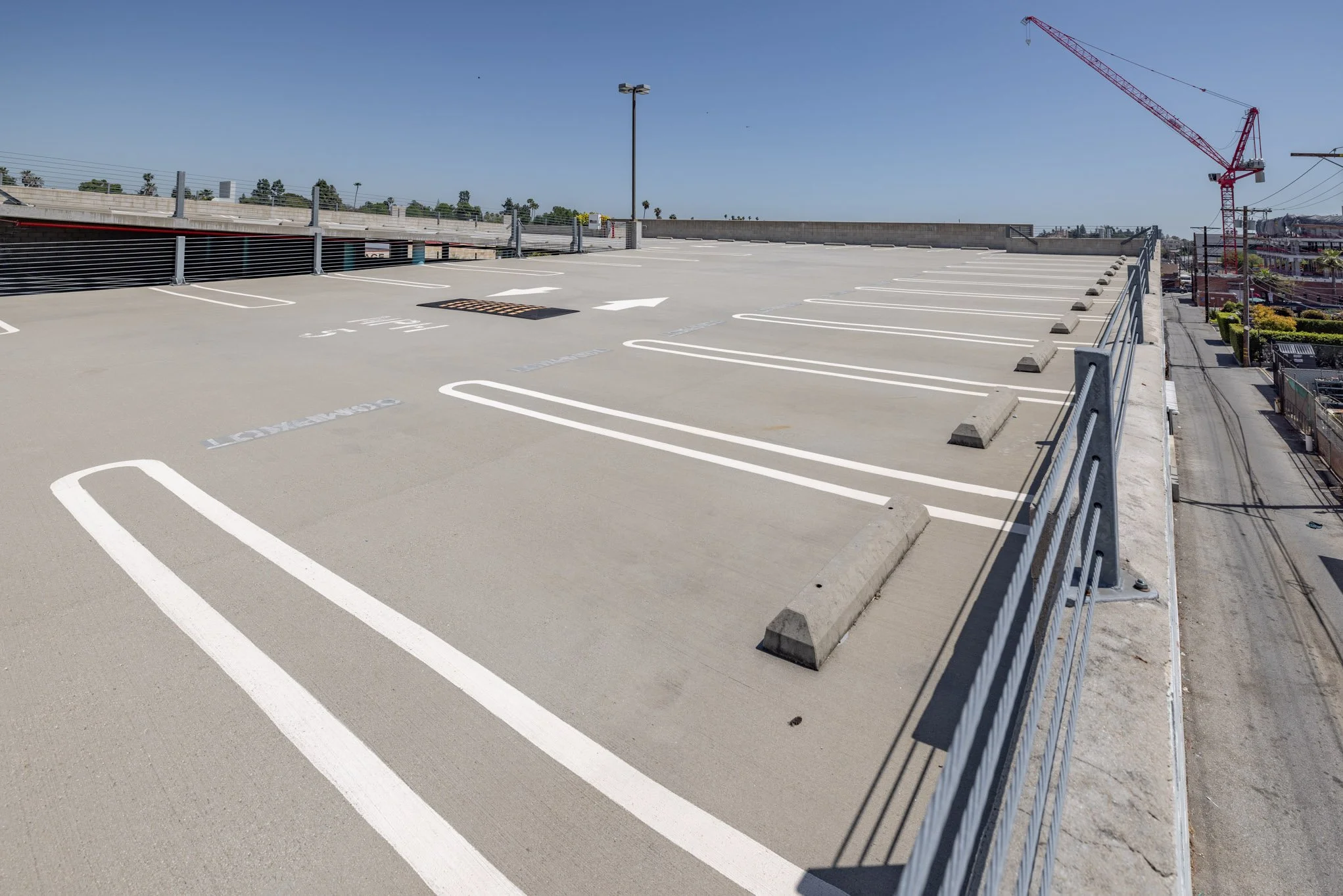 Empty rooftop parking lot with white marked parking spaces and barriers, under clear blue sky.