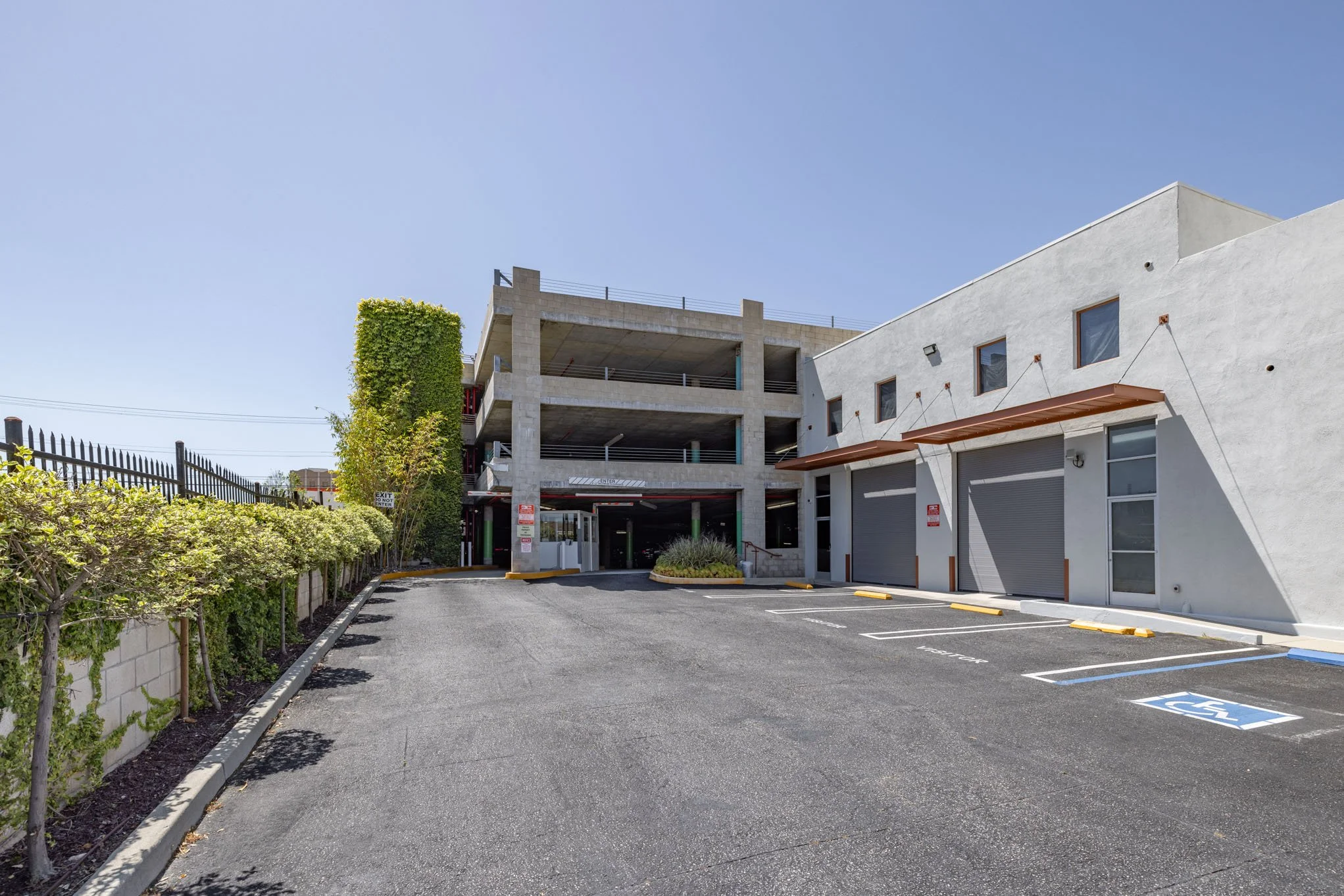 Empty parking lot with handicapped space, adjacent to a white building and an unfinished parking garage.