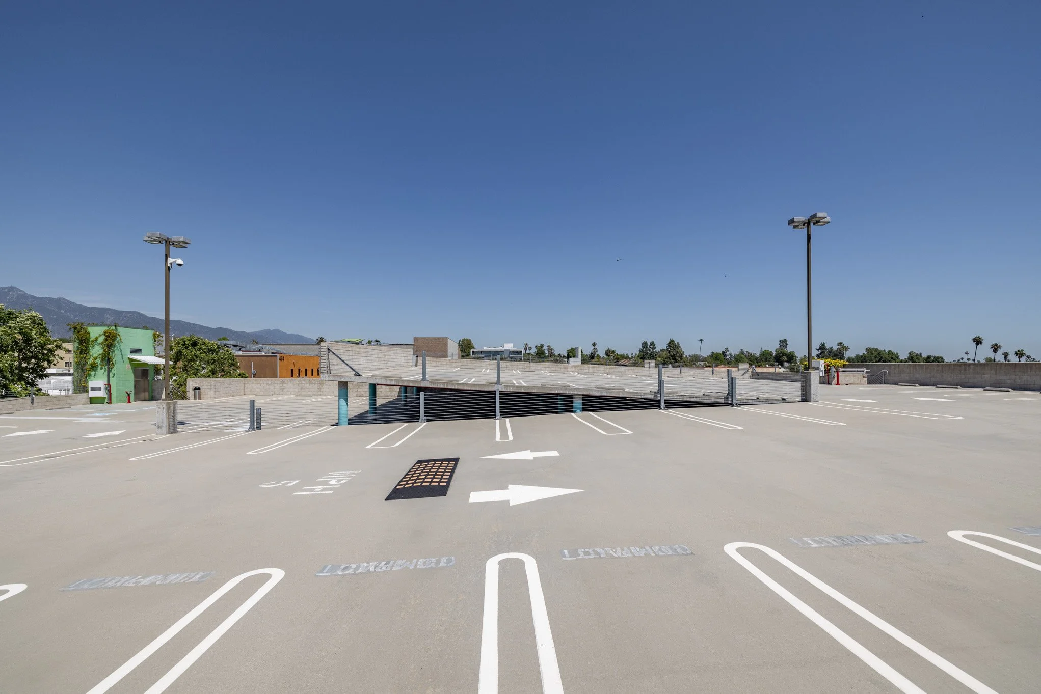 Empty outdoor parking garage with clear sky, marked parking spaces, directional arrows, and surrounding buildings.