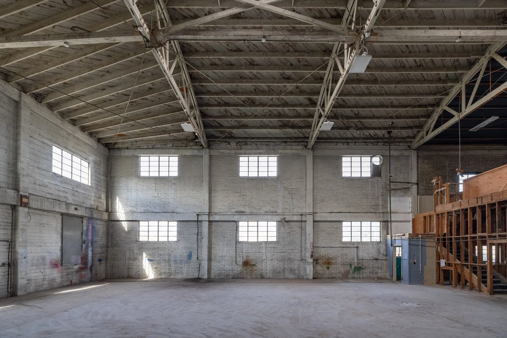 Empty industrial warehouse with white brick walls, large windows, and a high ceiling with exposed beams.