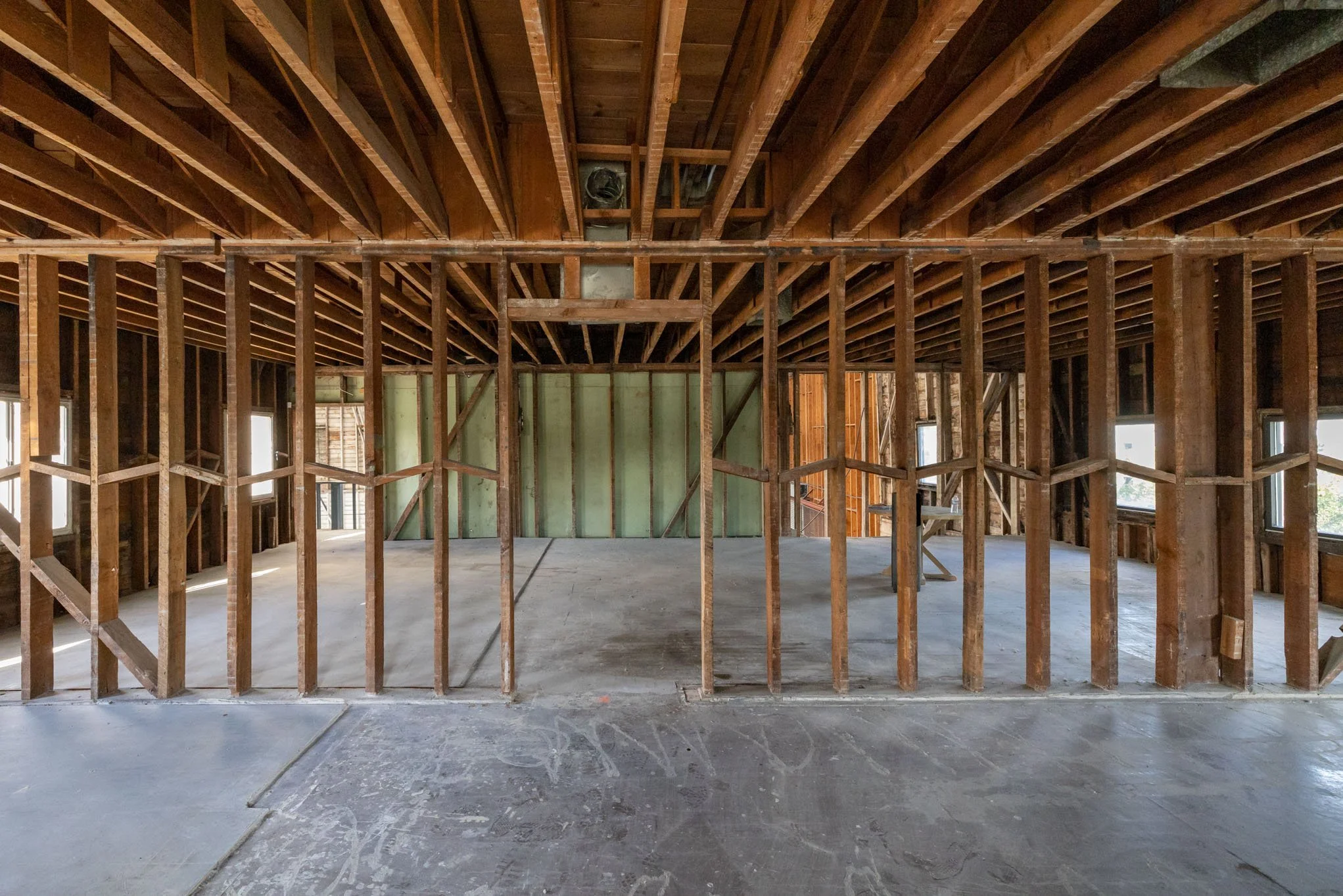 Interior of a house under construction with exposed wooden framing, support beams, and an unfinished concrete floor.