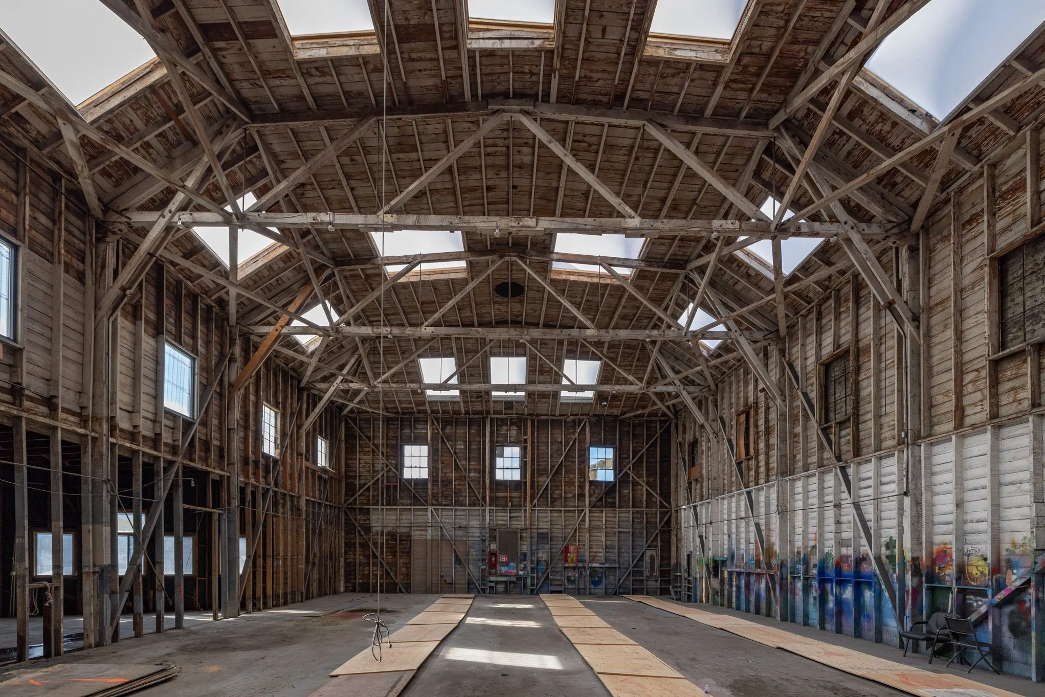 Large unfinished barn with wooden walls and ceiling, multiple windows, and construction materials on the ground.