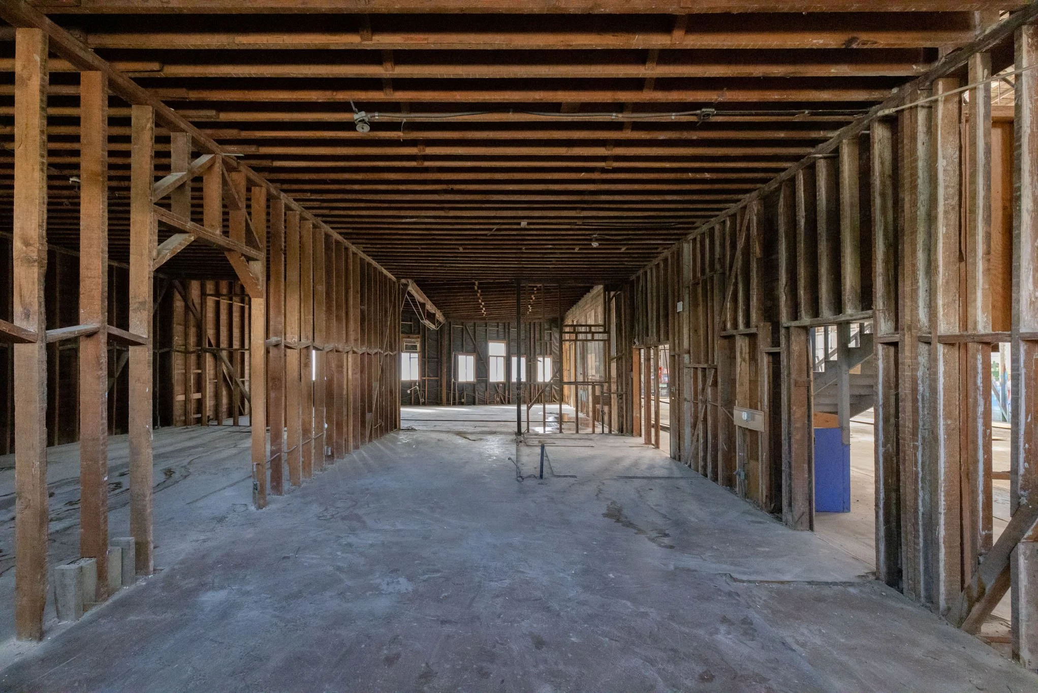 Interior of a building under construction with exposed wooden framing and a concrete floor.
