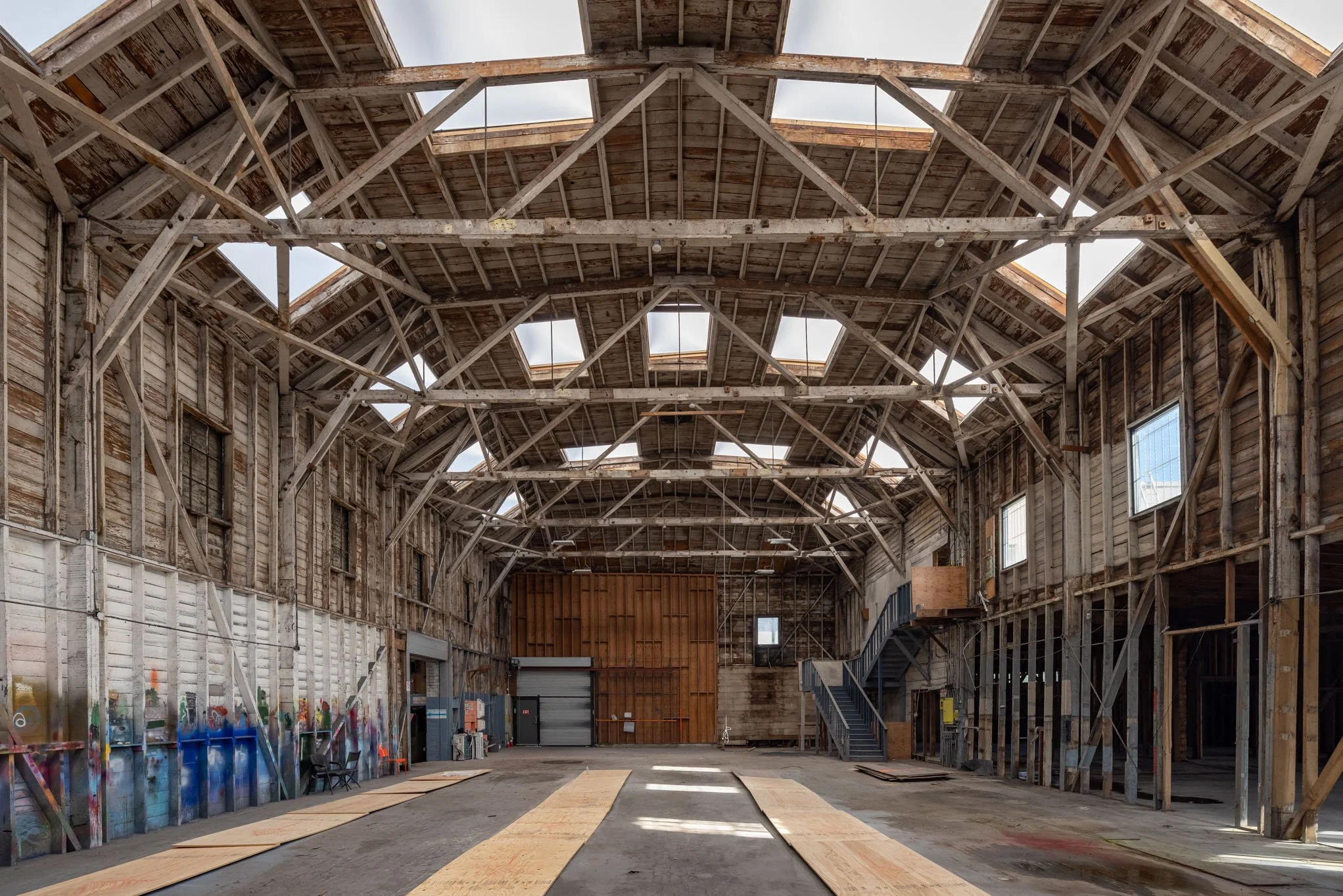 Empty warehouse with exposed wooden beams, missing ceiling panels, and a large garage door at the back.