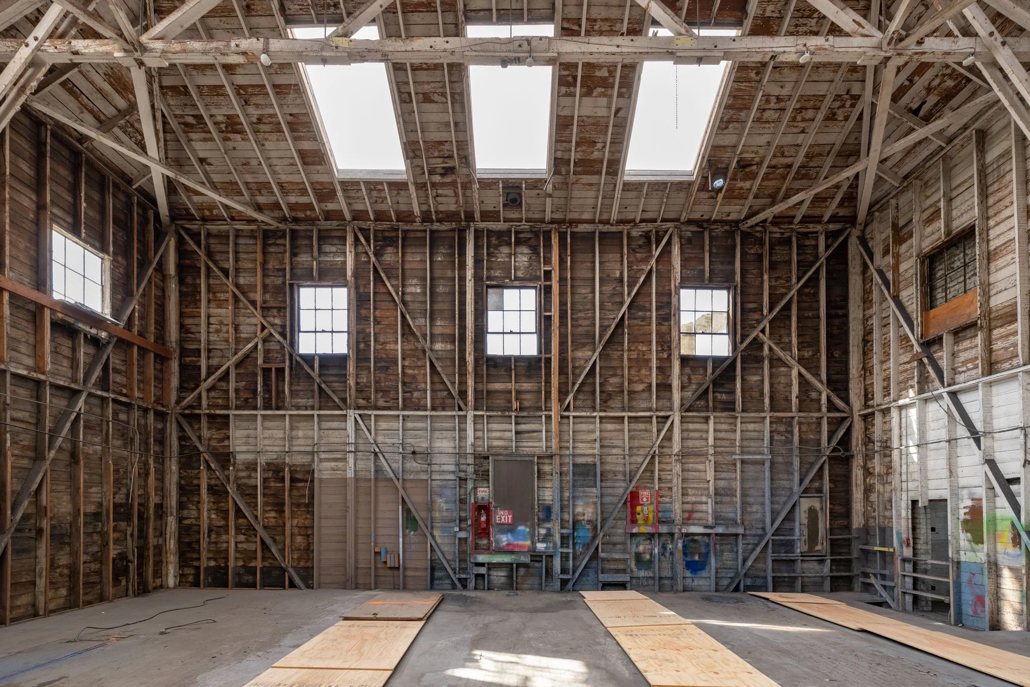 Interior of an unfinished building with exposed wooden framework and four skylights on the ceiling.
