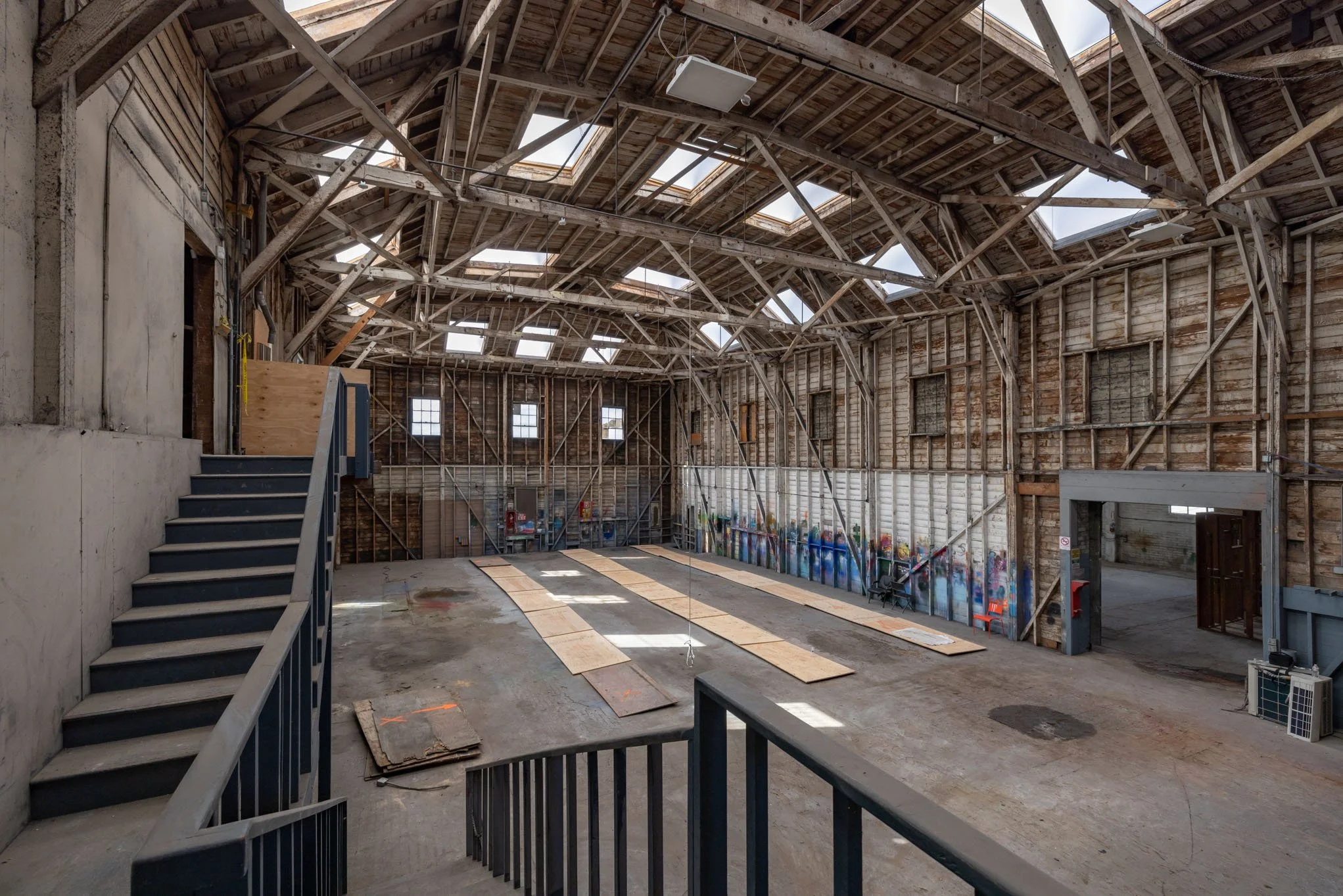 Interior of an old, partially renovated barn with exposed wooden beams, skylights, graffiti on the walls, and construction materials on the floor.