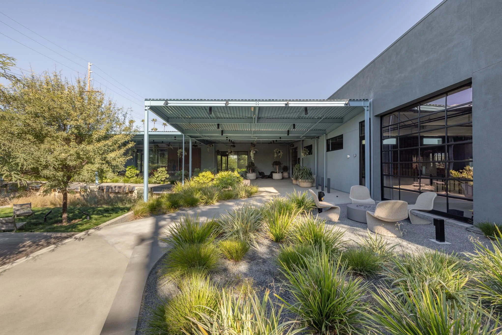 Modern outdoor patio with beige seating, green landscaping, and a shaded area attached to a light blue building.