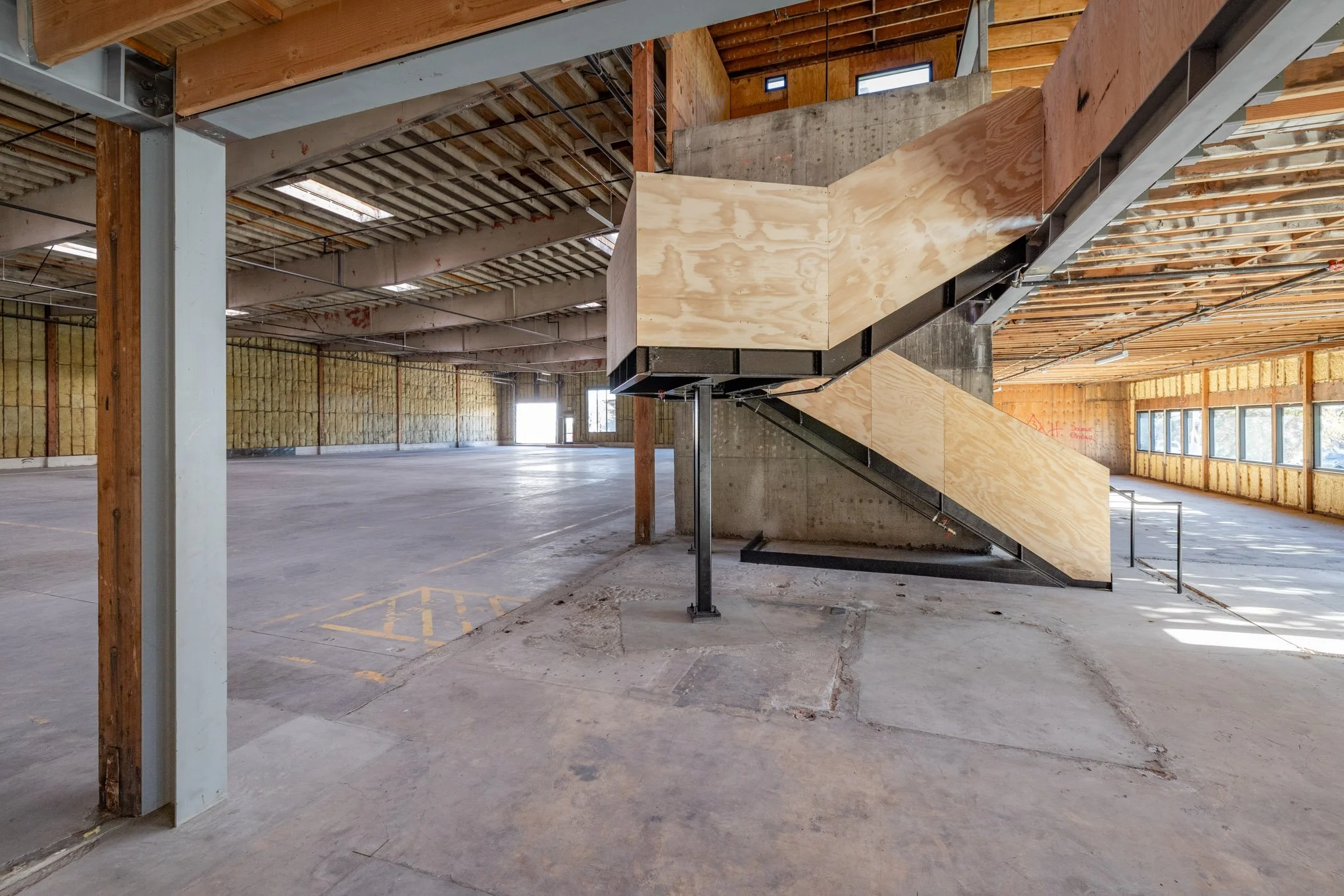 Under construction or renovation interior space with unfinished walls, exposed ceiling beams, and a new wooden staircase with black metal supports.