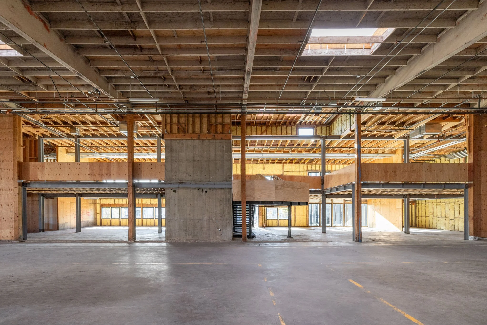 Empty building interior under construction with exposed wooden beams, concrete walls, and metal support structures.