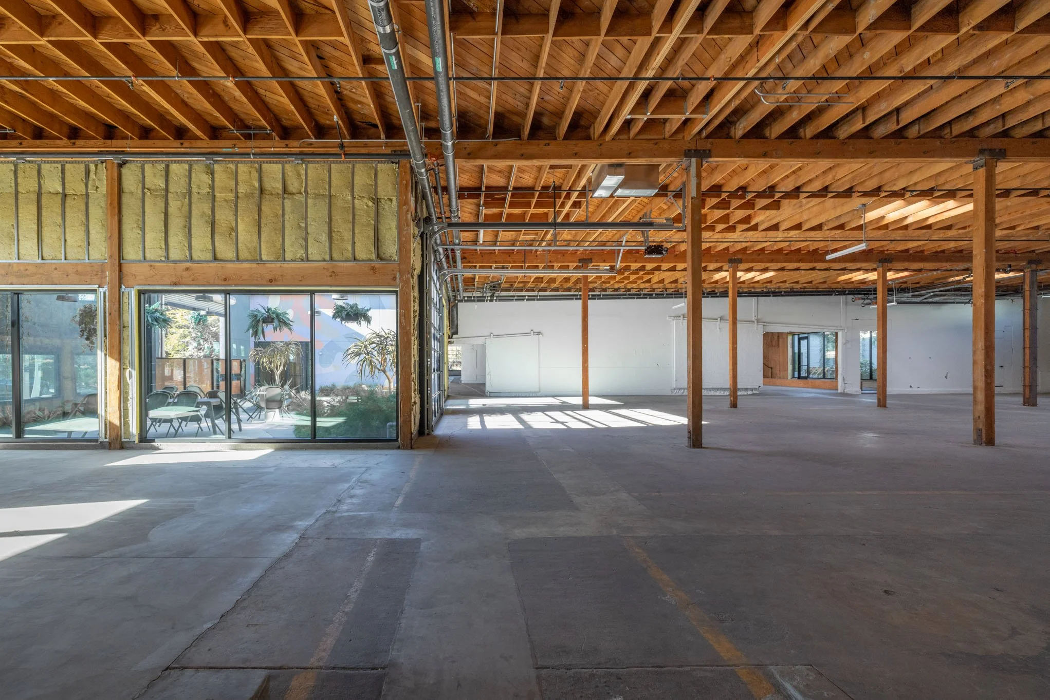 Empty interior of a commercial space or warehouse with exposed wooden beams and large glass windows.