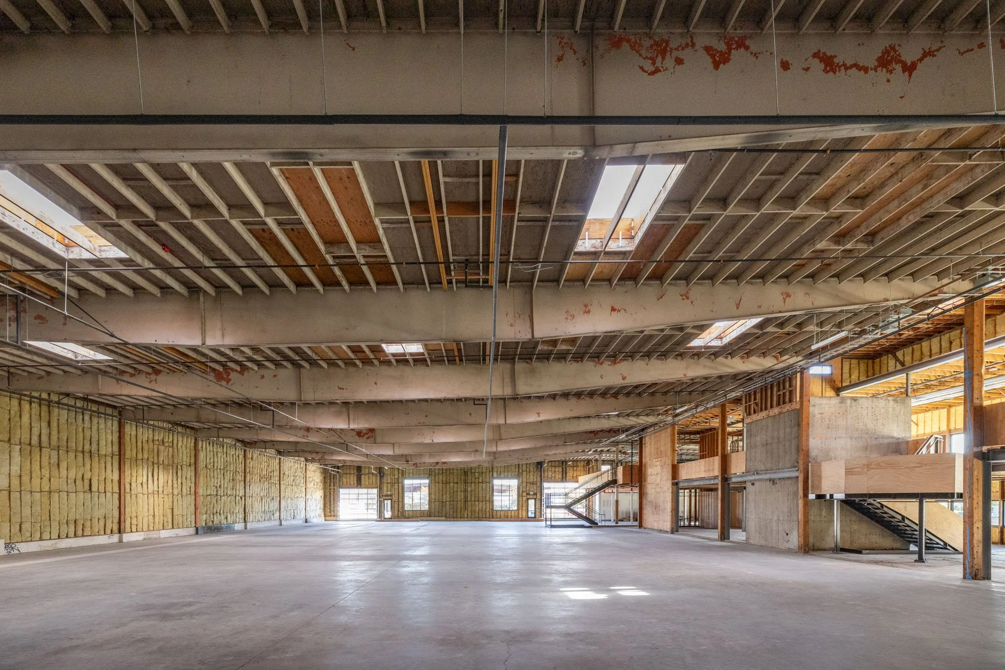 Interior of an unfinished commercial building with exposed ceiling beams, insulation on the walls, and large open floor space.