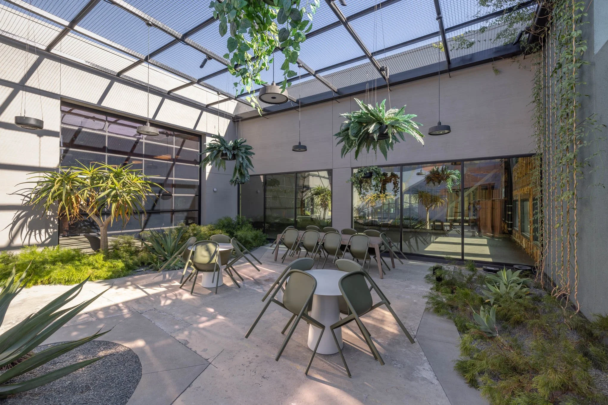 Indoor patio with modern decor, natural light, hanging plants, and various chairs around tables, surrounded by greenery.
