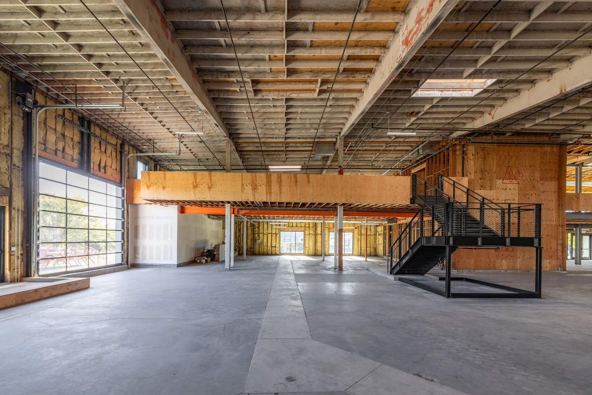 Interior of a building under construction with exposed ceiling, unfinished walls, and black metal stairs.
