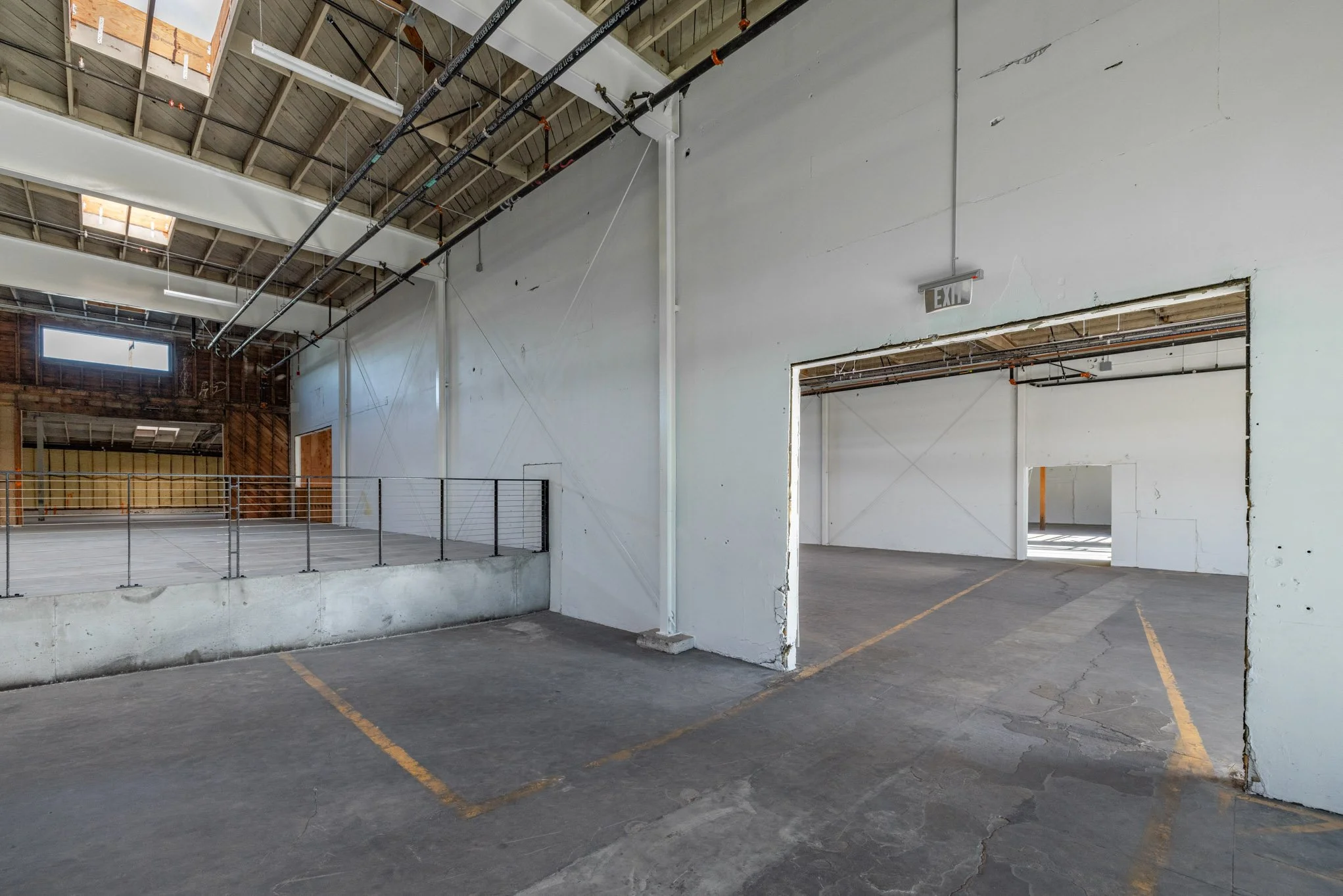 Empty industrial or warehouse space with concrete floors, white walls, and an open doorway leading to another section of the building.