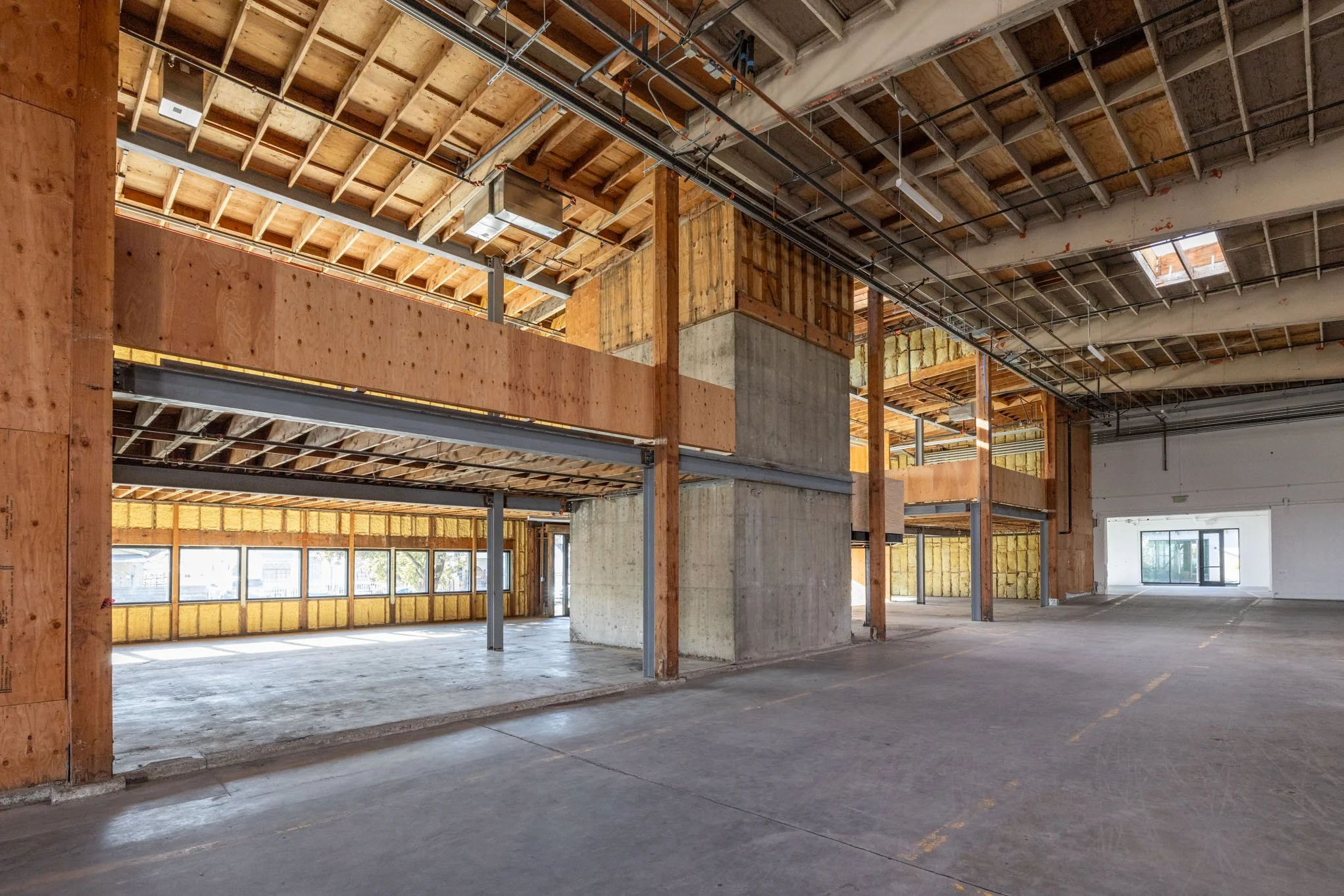  Interior of a building under construction with exposed wooden beams, concrete walls, and large windows.