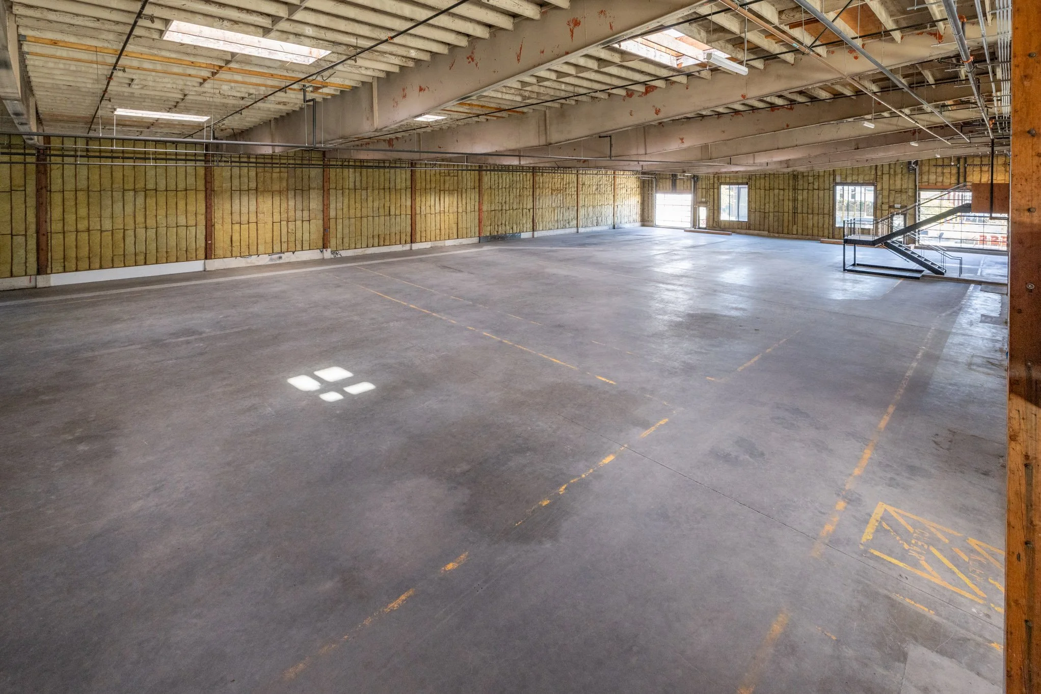 Empty multi-level parking garage with concrete floors, partially constructed walls, and natural light coming through skylights and windows.