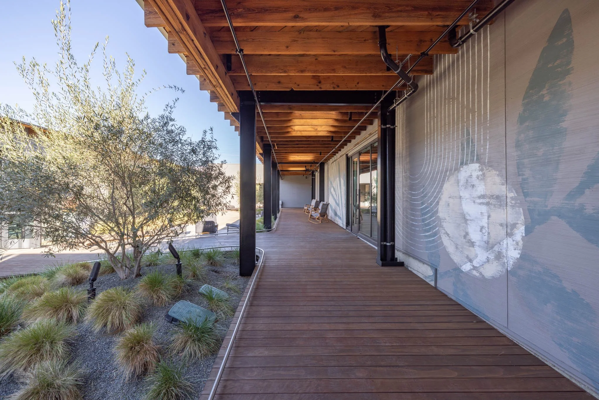 Outdoor wooden balcony with seating overlooking a landscaped area with trees and plants